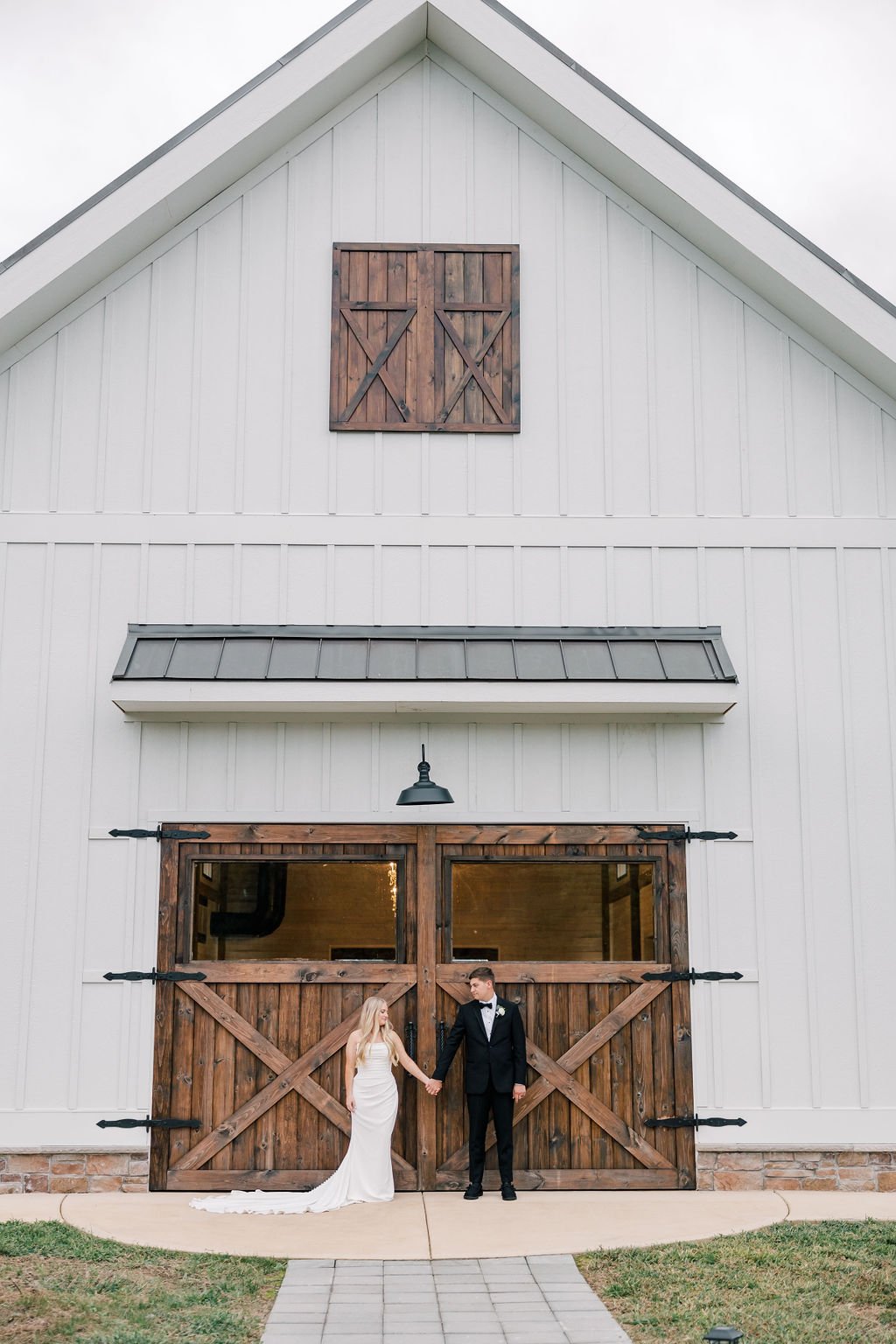 Bride and groom holding hands in front of a large rustic barn with wooden double doors and a white exterior