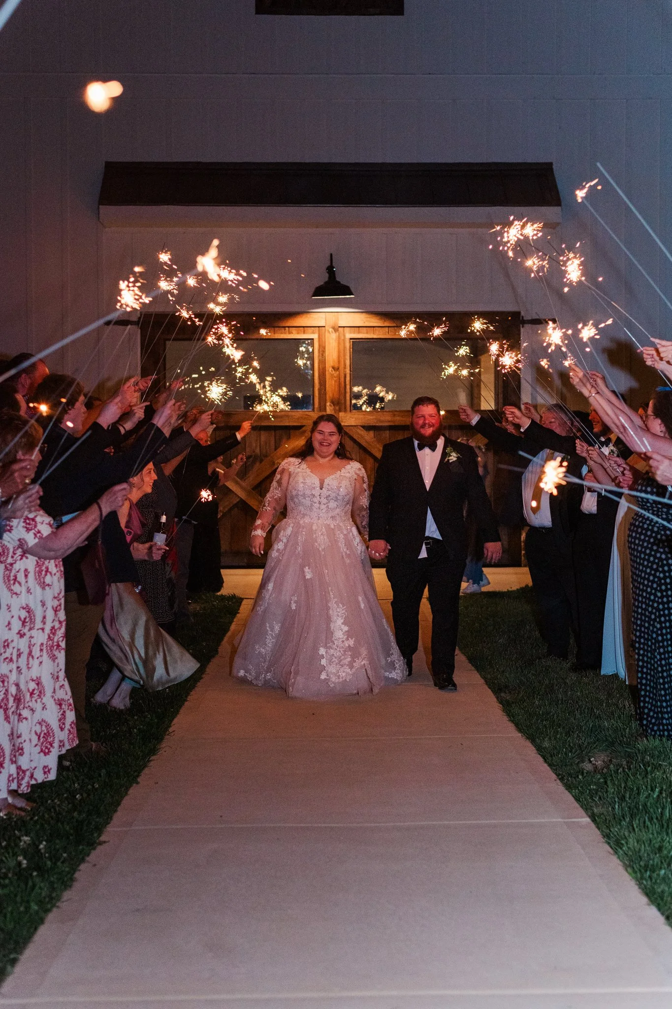 Bride and groom walking hand-in-hand through a sparkler exit with friends and family on either side.