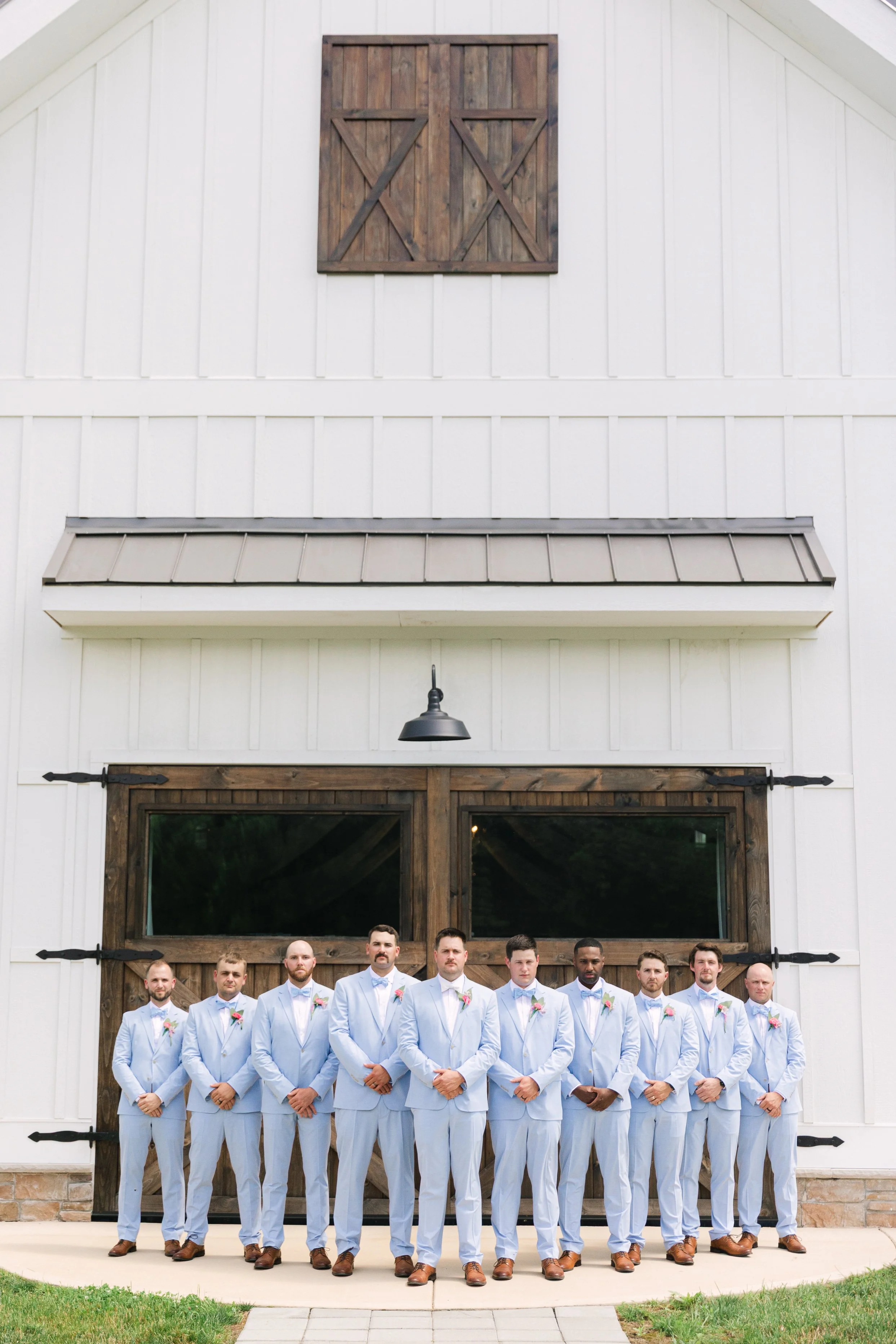 Group of men dressed in light blue suits standing in front of a white barn with dark wood accents.