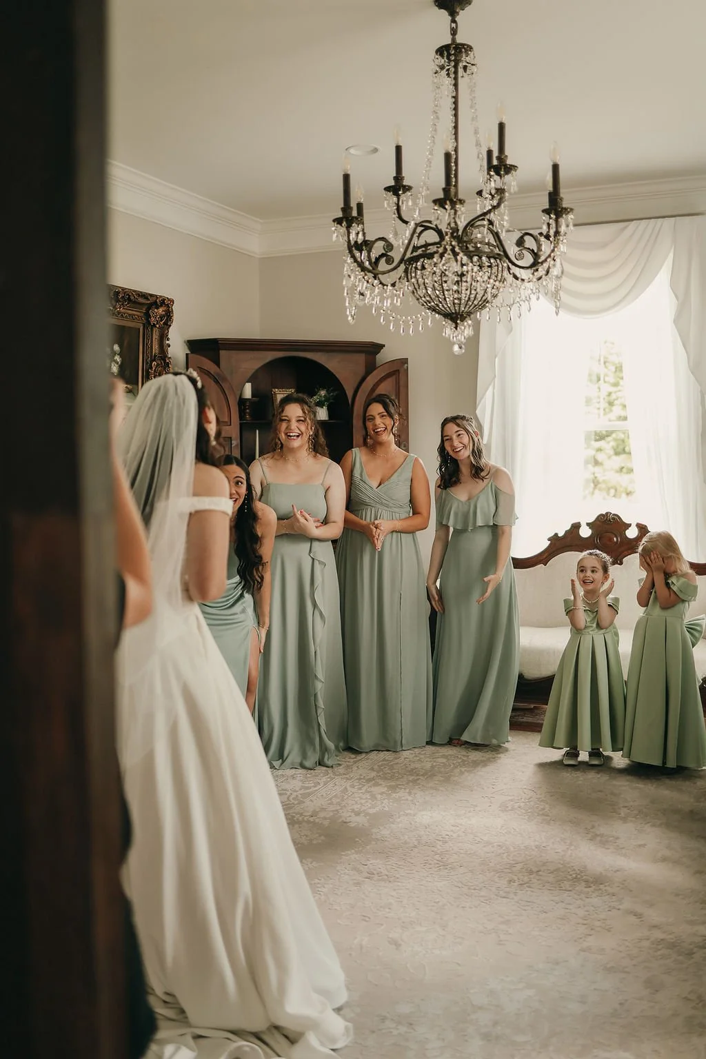 Bride and bridesmaids in a well-decorated room with a chandelier, enjoying a joyful moment before the wedding.