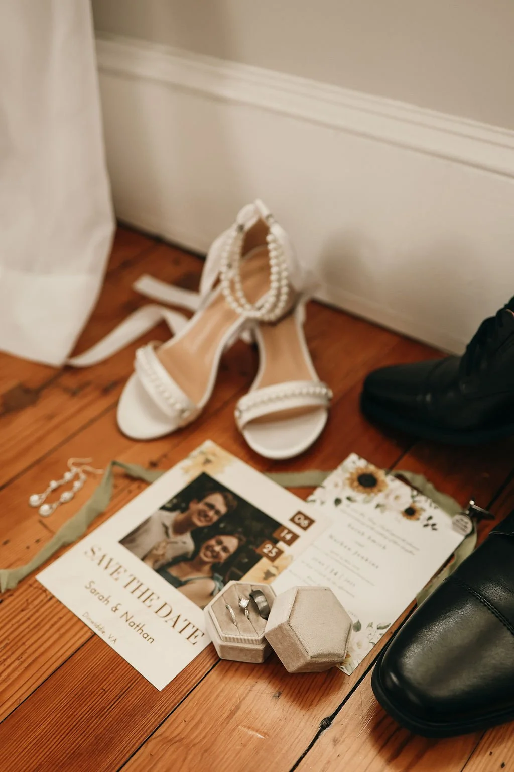 Groom's wedding shoes, a wedding invitation, jewelry, and a photo of a happy couple on a wooden floor.