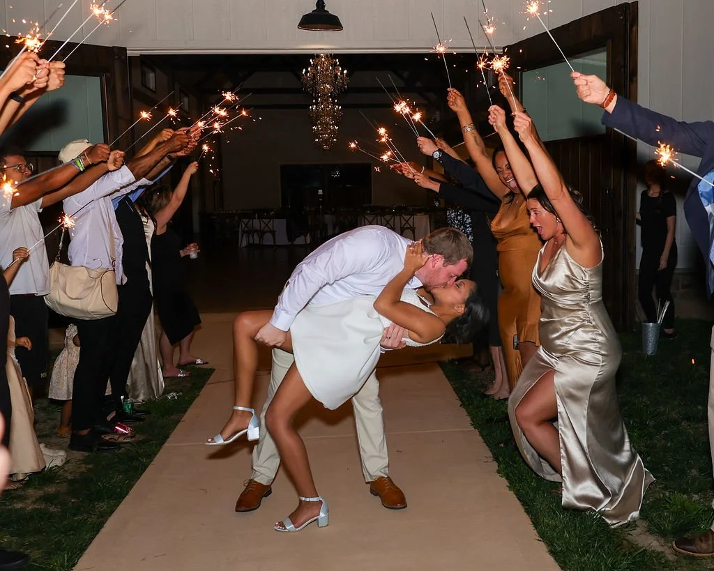 A bride and groom sharing a kiss while dancing at a celebration, surrounded by guests holding sparklers.