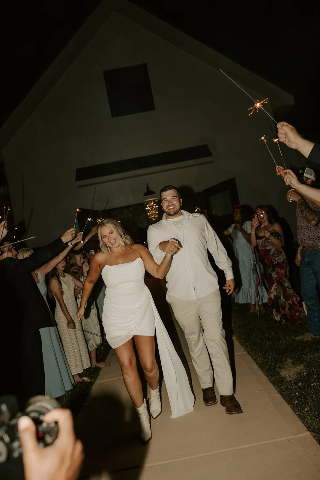 Couple walking down aisle at night, surrounded by friends holding sparklers, celebrating at a wedding reception.