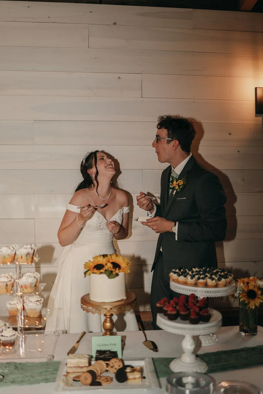 A bride and groom at their wedding reception, sharing a moment by the cake table, surrounded by desserts and floral decorations.
