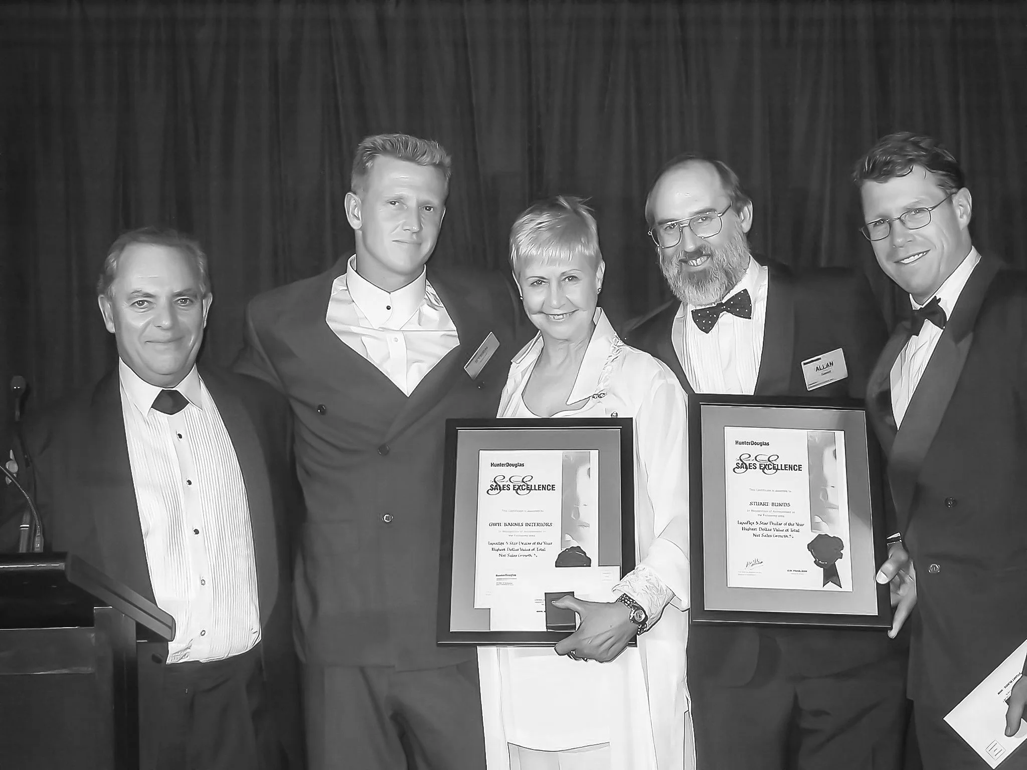 Five people in formal attire at an award ceremony, holding framed certificates and smiling for the photo.
