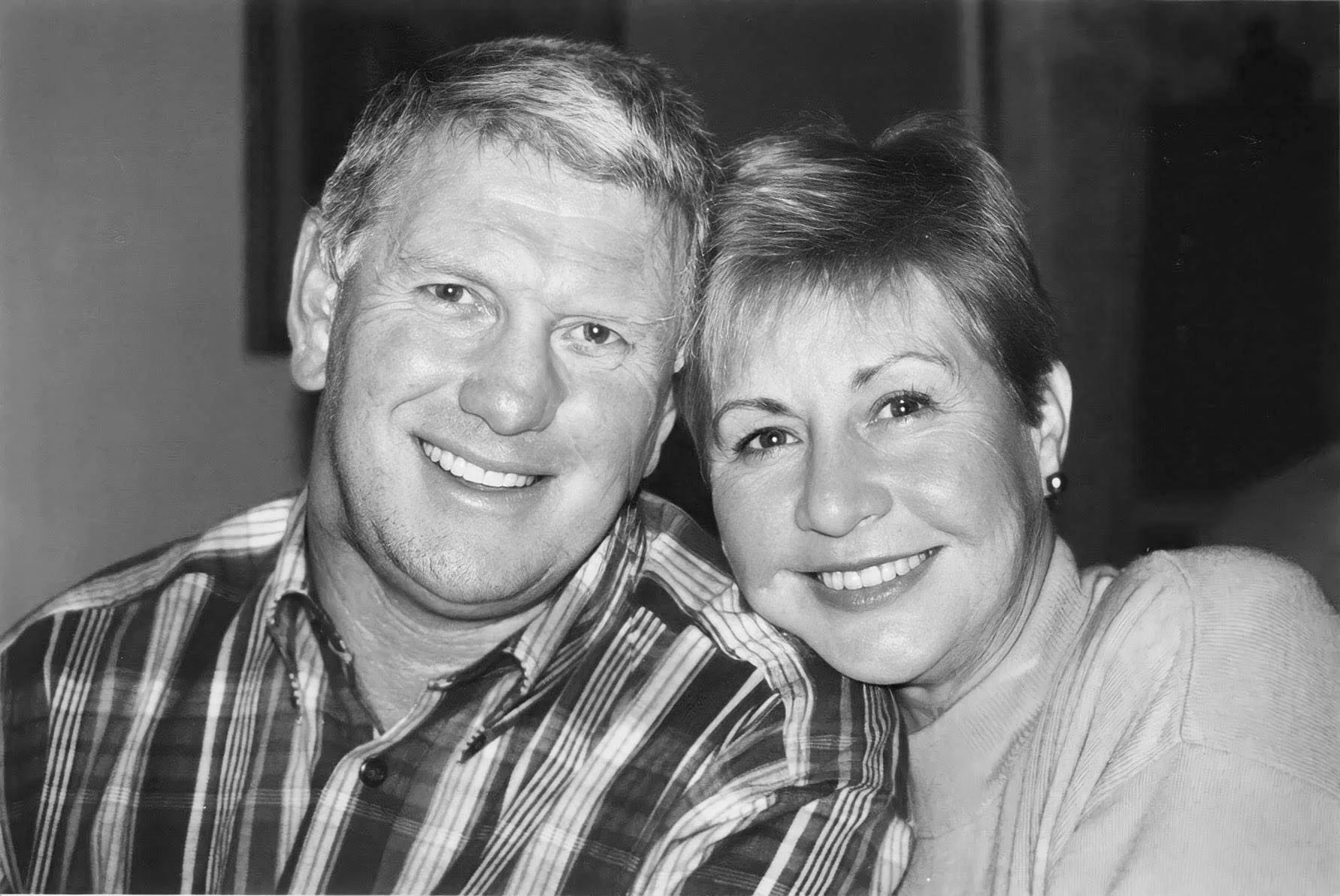 A black and white photo of a smiling middle-aged man and woman close together, looking at the camera.
