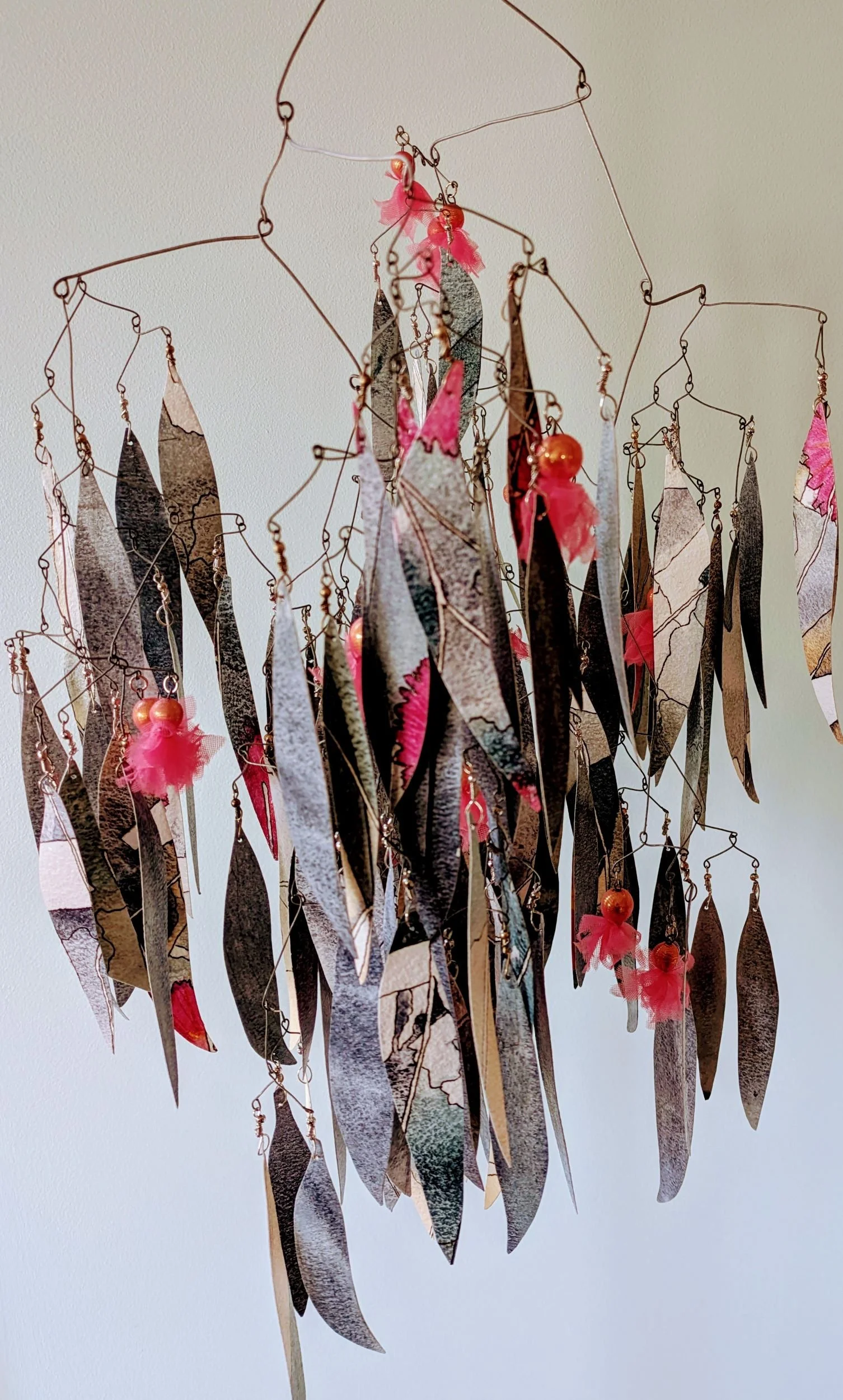 Hanging kinetic sculpture representing the leaves and blossoms of the ironbark tree, made from painted and sealed watercolour paper, beads covered in pink fabric as blossoms and a metal wire frame.