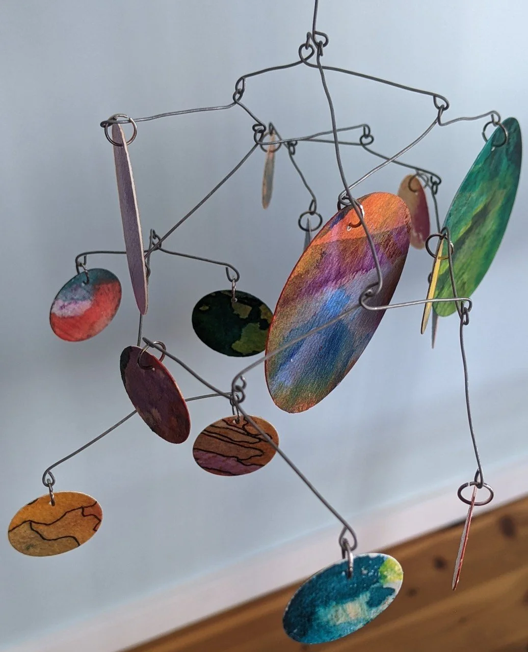 Mobile with colorful painted circular and oval wooden pieces hanging from thin wire