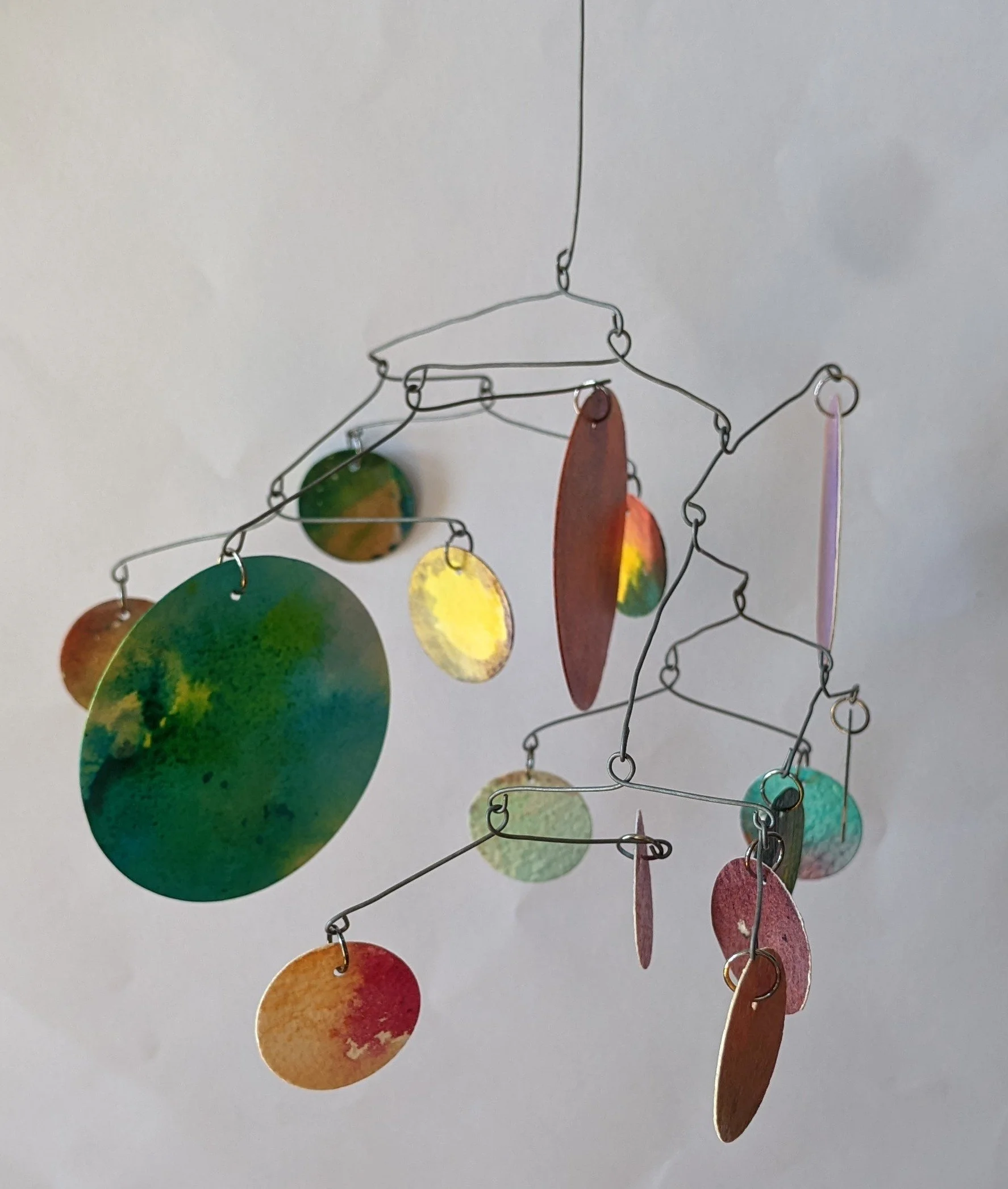Colorful abstract mobile with different sized circular pieces of painted and sealed watercolour paper hanging from thin wire.