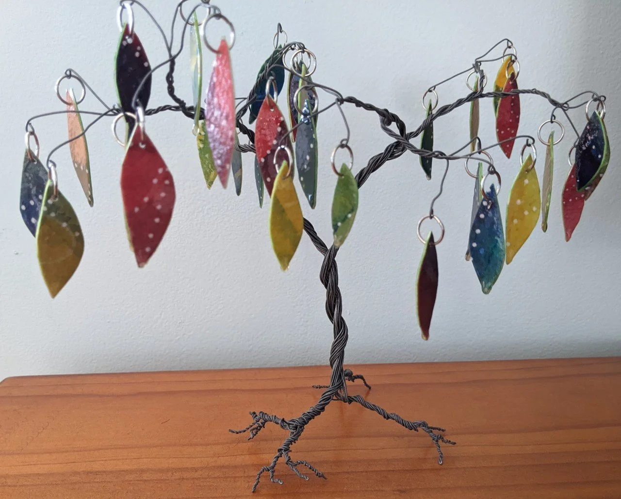 A decorative wire tree with colorful leaves made from painted and resined watercolour paper hanging from its branches.