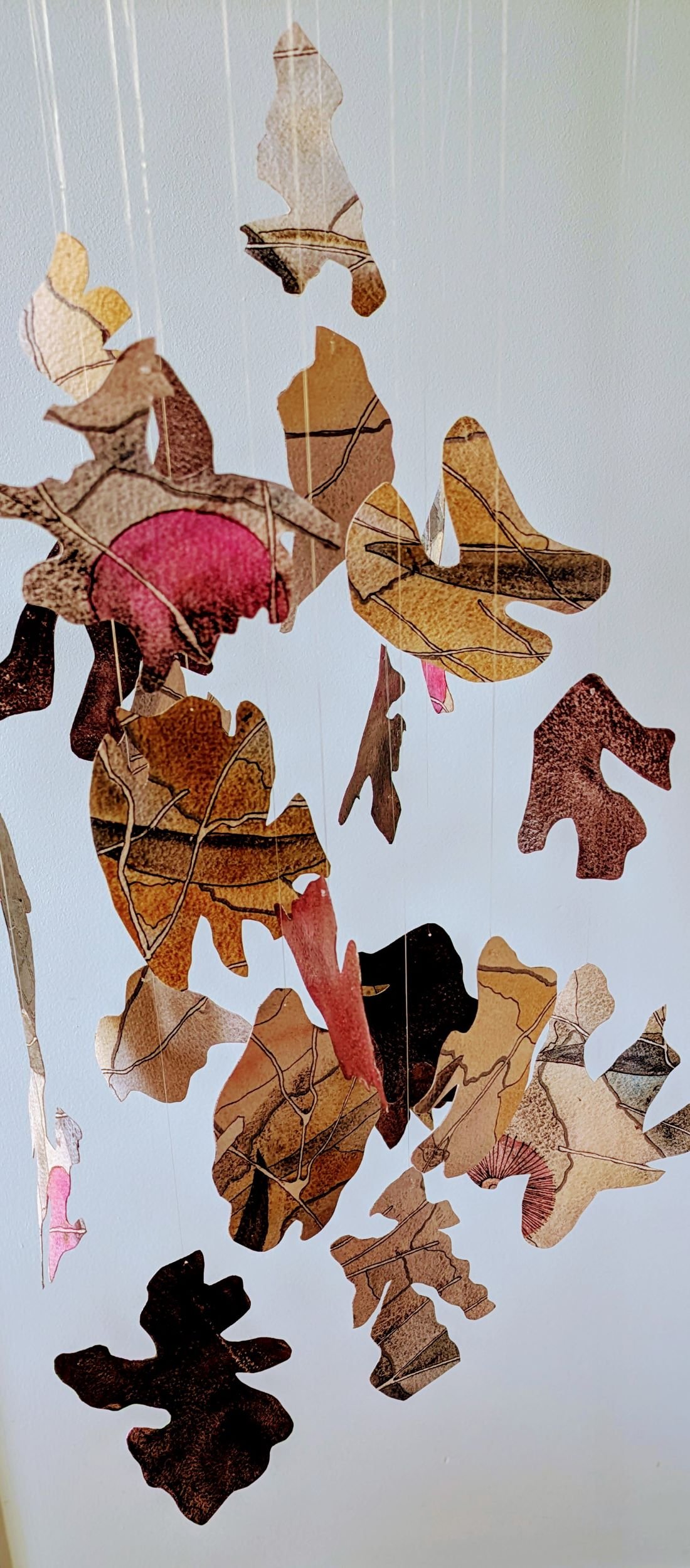 Hanging kinetic sculpture  made of cutout shapes of painted and sealed watercolour paper, representing mulch and debris that falls to the ground, suspended by thin string lines.