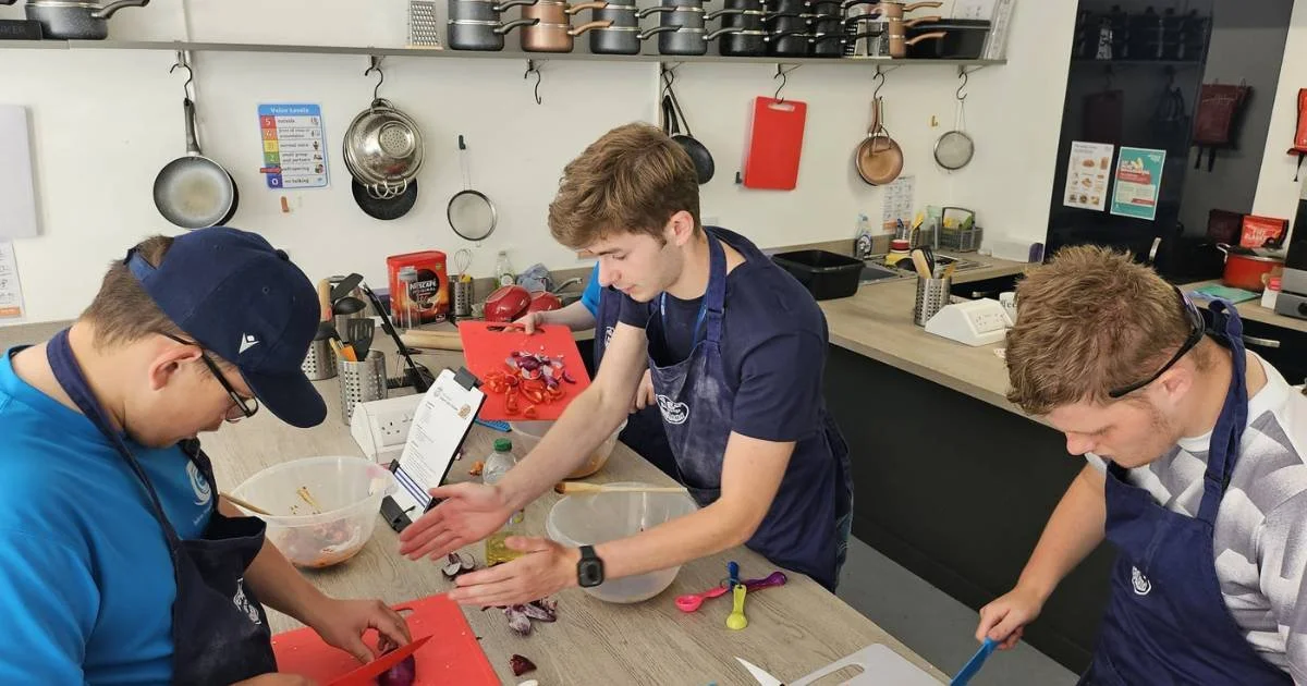 Young adults preparing food together in a teaching kitchen, developing practical cooking skills and independence