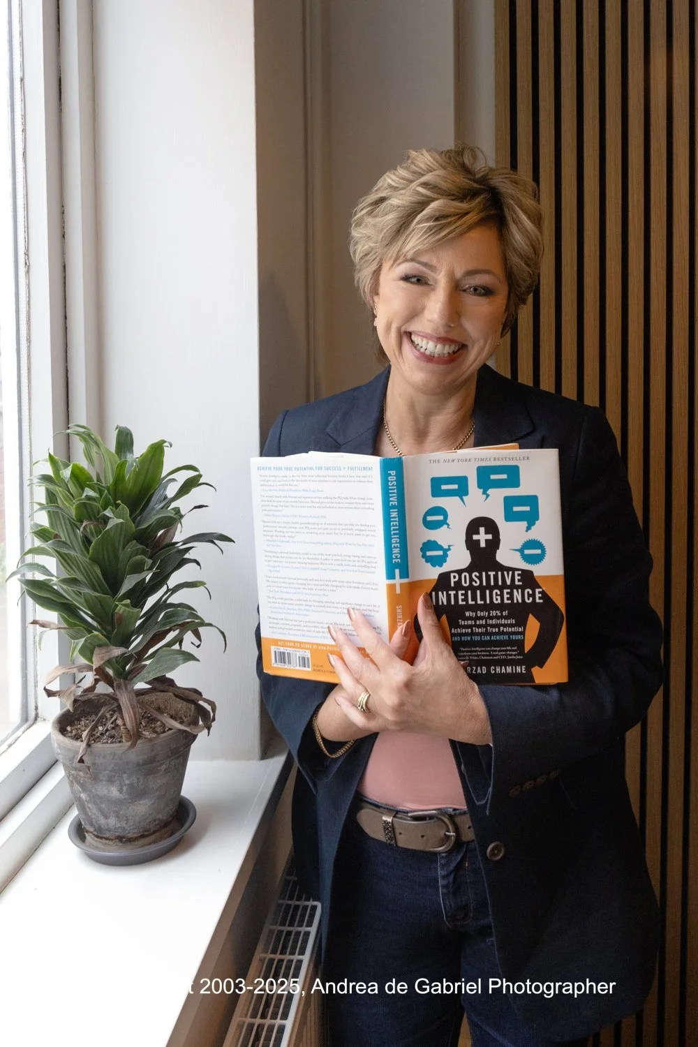 Personal Branding Photography at Exeter Quay by Cornwall Branding Photography. Woman standing by window, smiling and holding the Emotional Intelligence book. 
