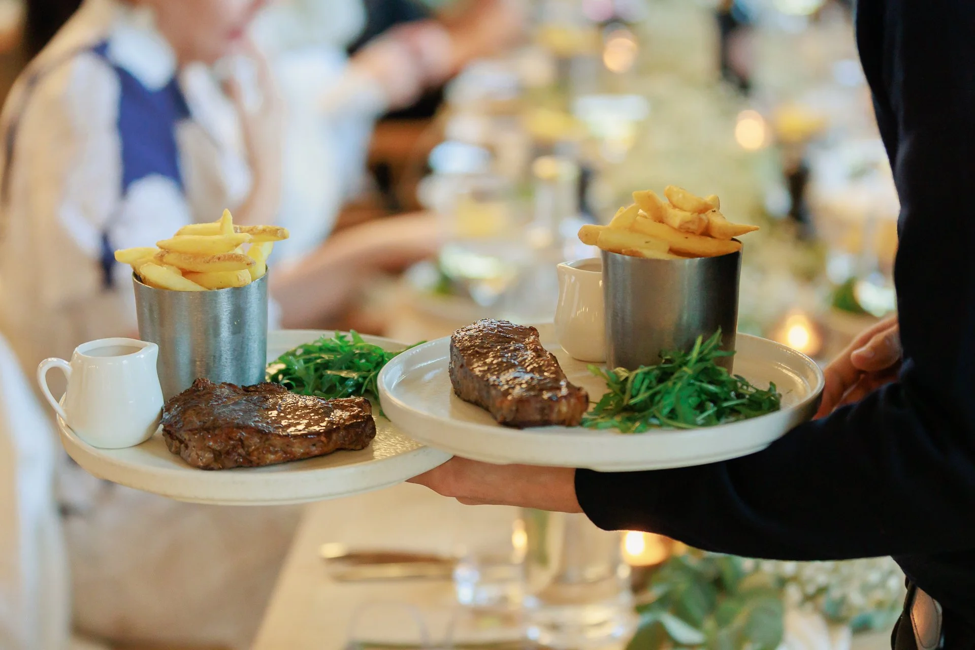 Person serving two plates with steak, French fries, and salad at a dinner event.