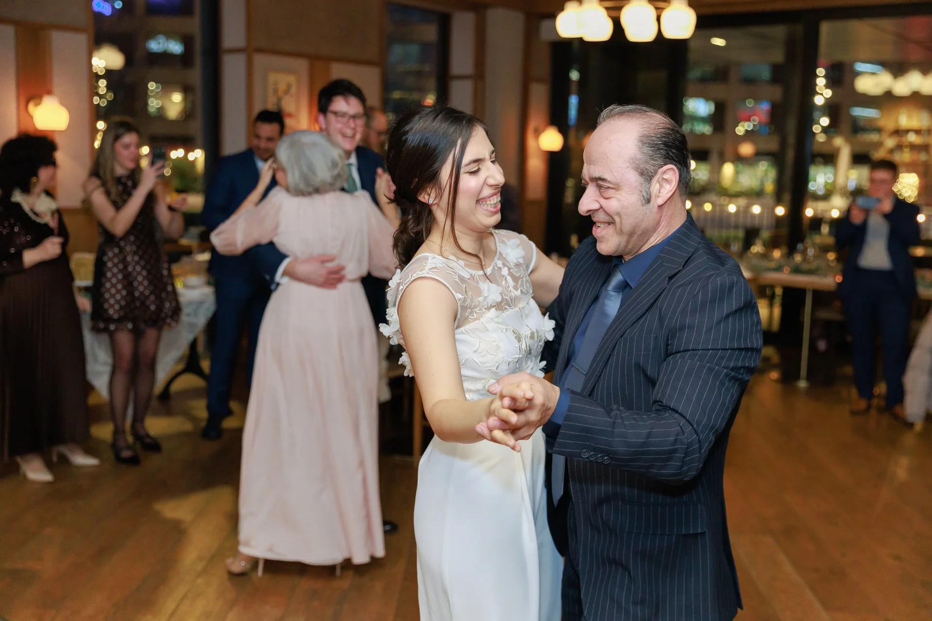 People dancing and celebrating at a wedding reception, with a woman in a white dress and a man in a suit dancing closely, surrounded by friends and family.