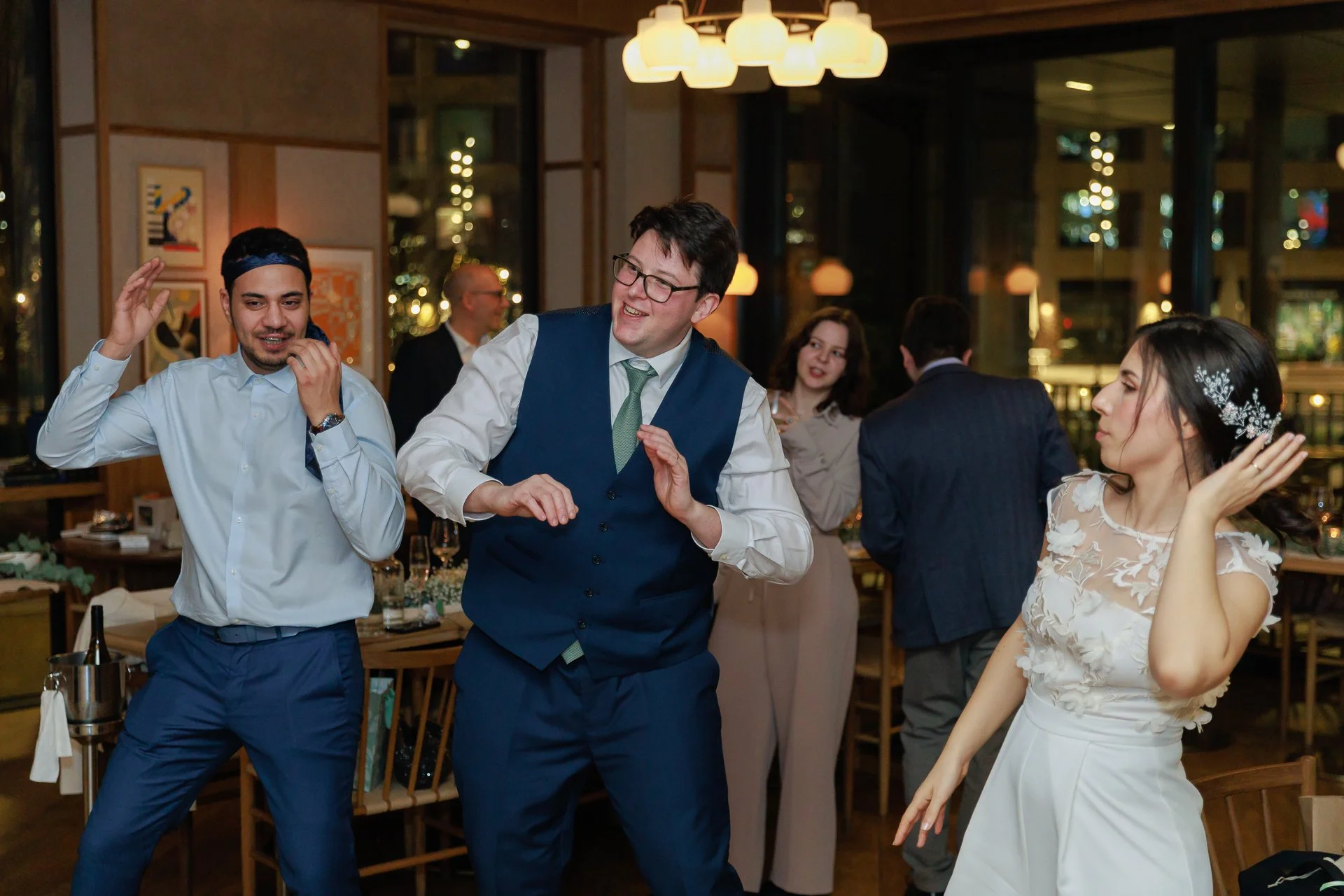 People dancing and celebrating at a social gathering or party in a warmly lit restaurant or banquet hall.