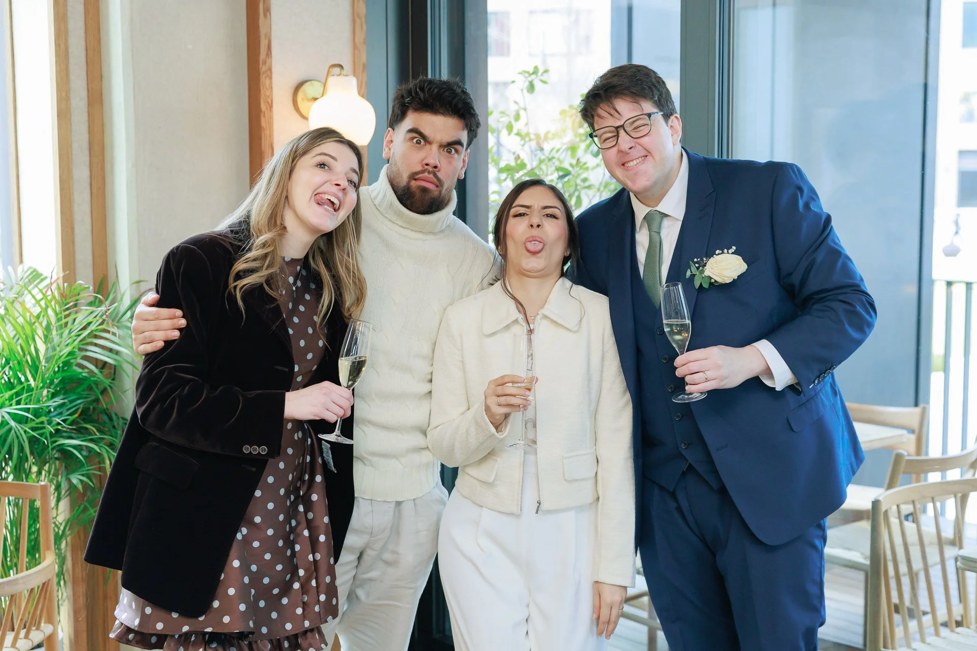 Four friends celebrating at a wedding reception, holding glasses of champagne and making funny faces.