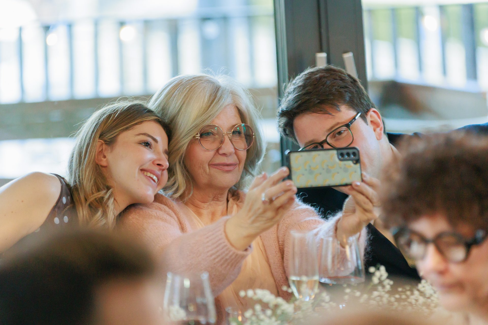 Three people, including an older woman and two younger adults, taking a selfie together at a social gathering, smiling happily.