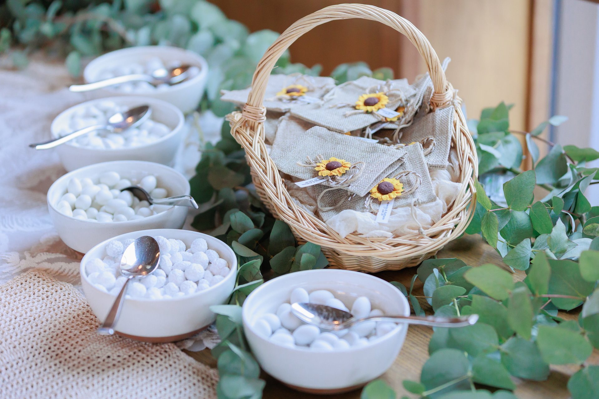 Display of small towels with sunflower embellishments in a wicker basket, surrounded by white candies, edible pearls, and decorative greenery.