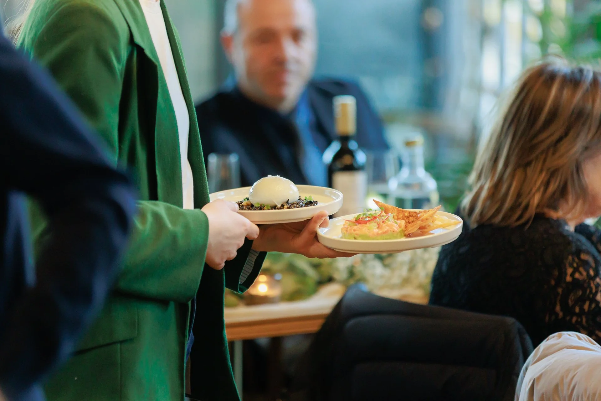 Waiter carrying plates of food in a restaurant with customers dining.