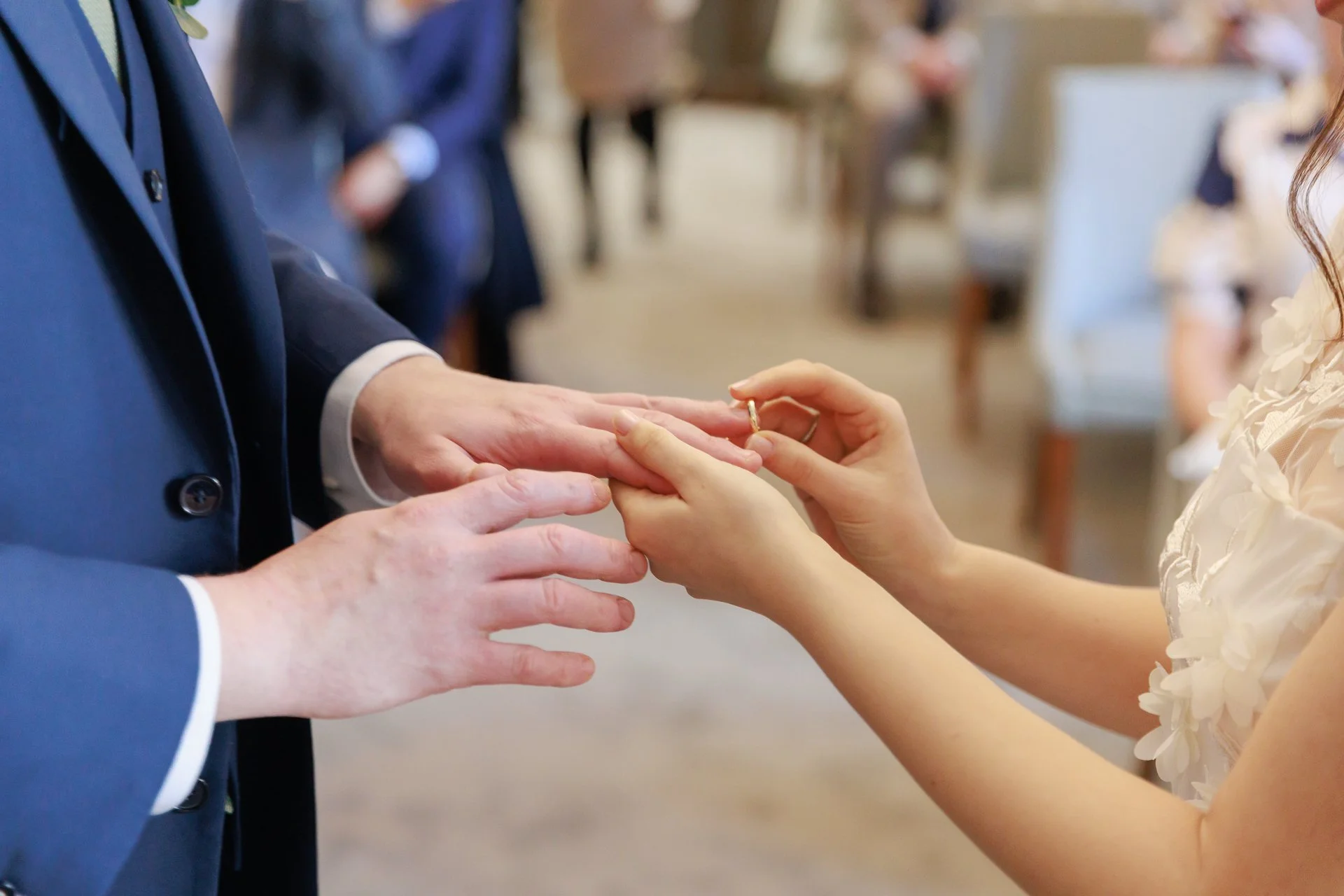 A couple exchanges wedding rings during their wedding ceremony, with the bride placing a ring on the groom's finger.