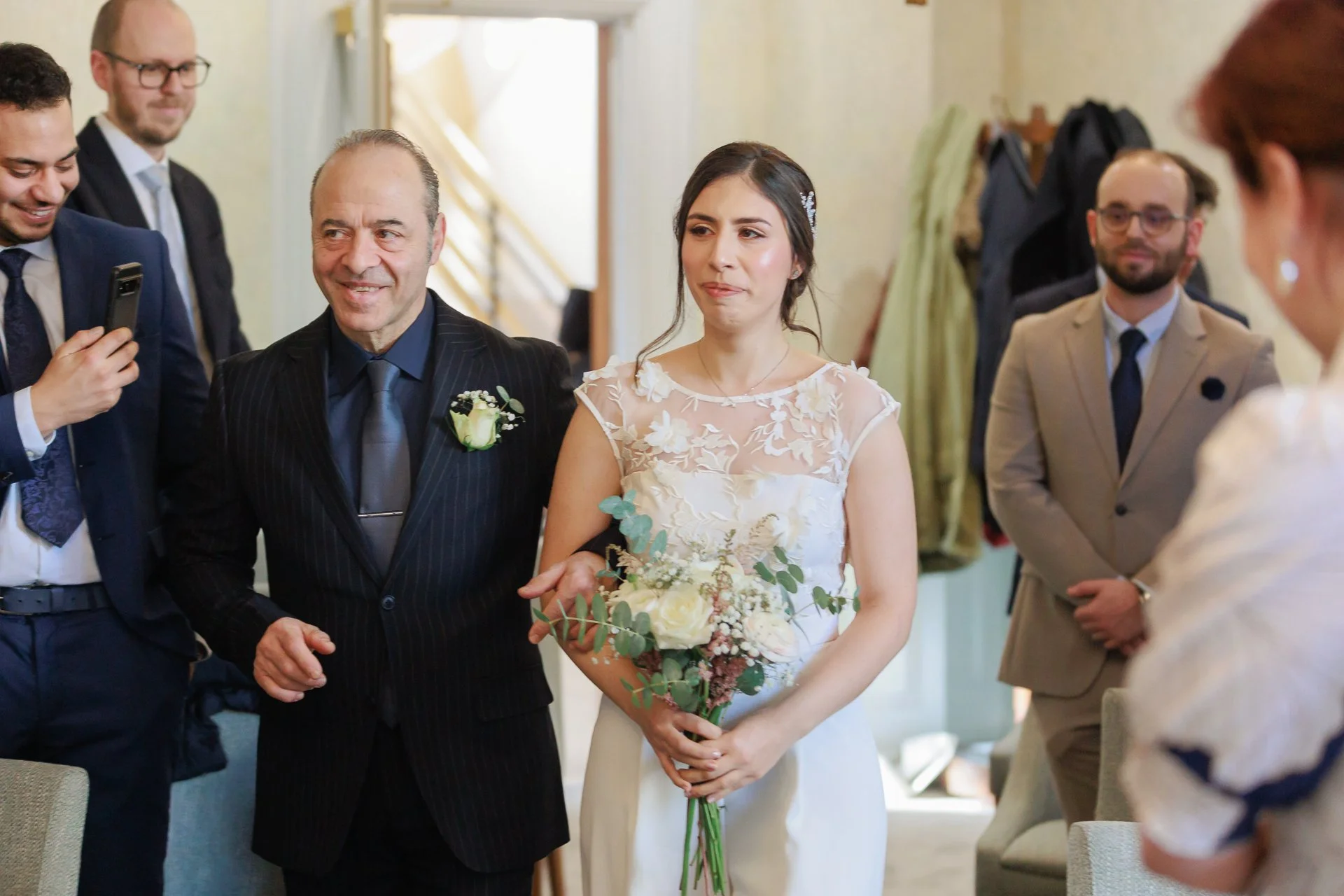 A bride holding a bouquet of white and pink flowers, surrounded by family and friends at a wedding ceremony