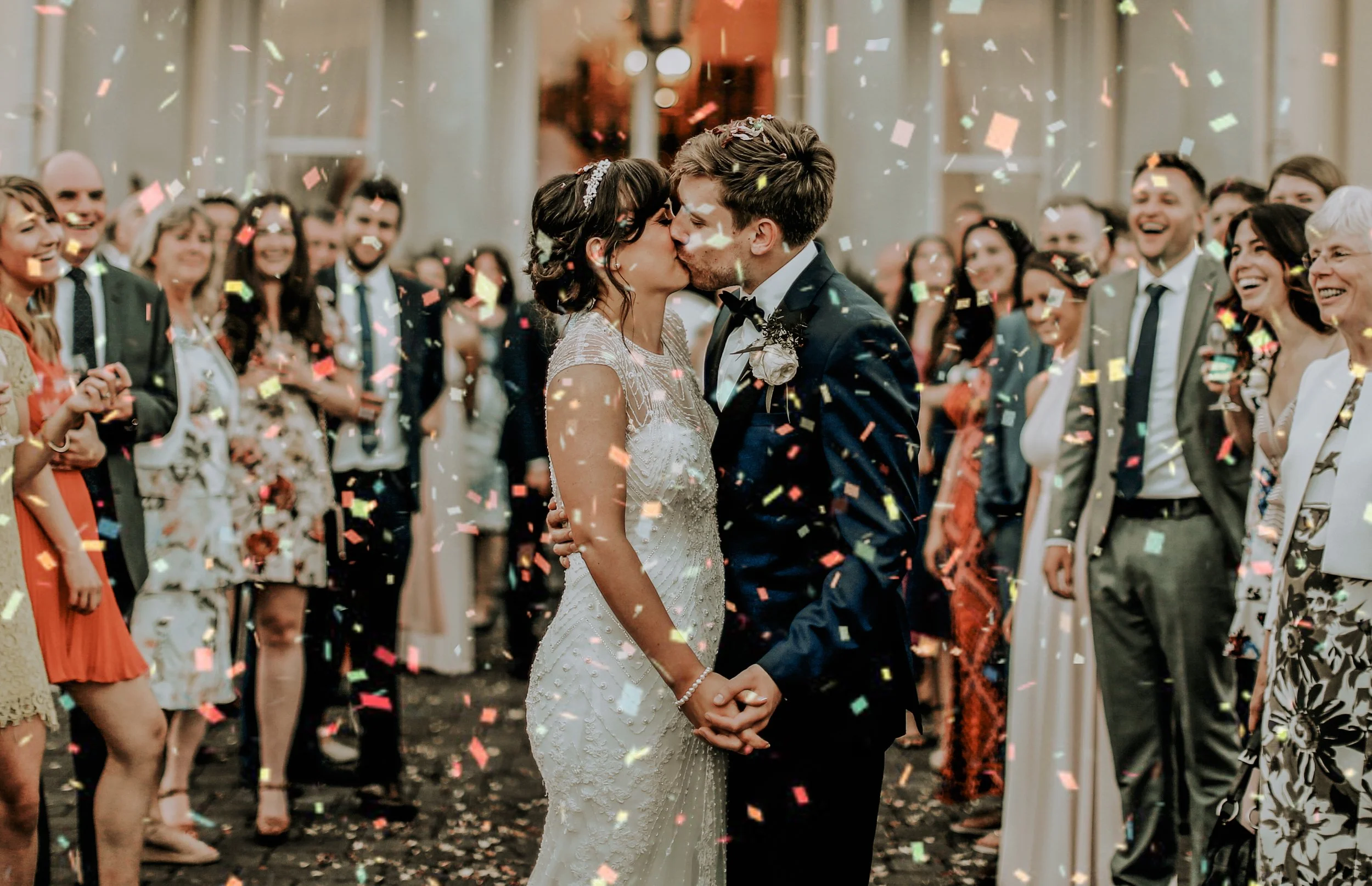 A bride and groom kiss during their wedding ceremony as guests celebrate with confetti.