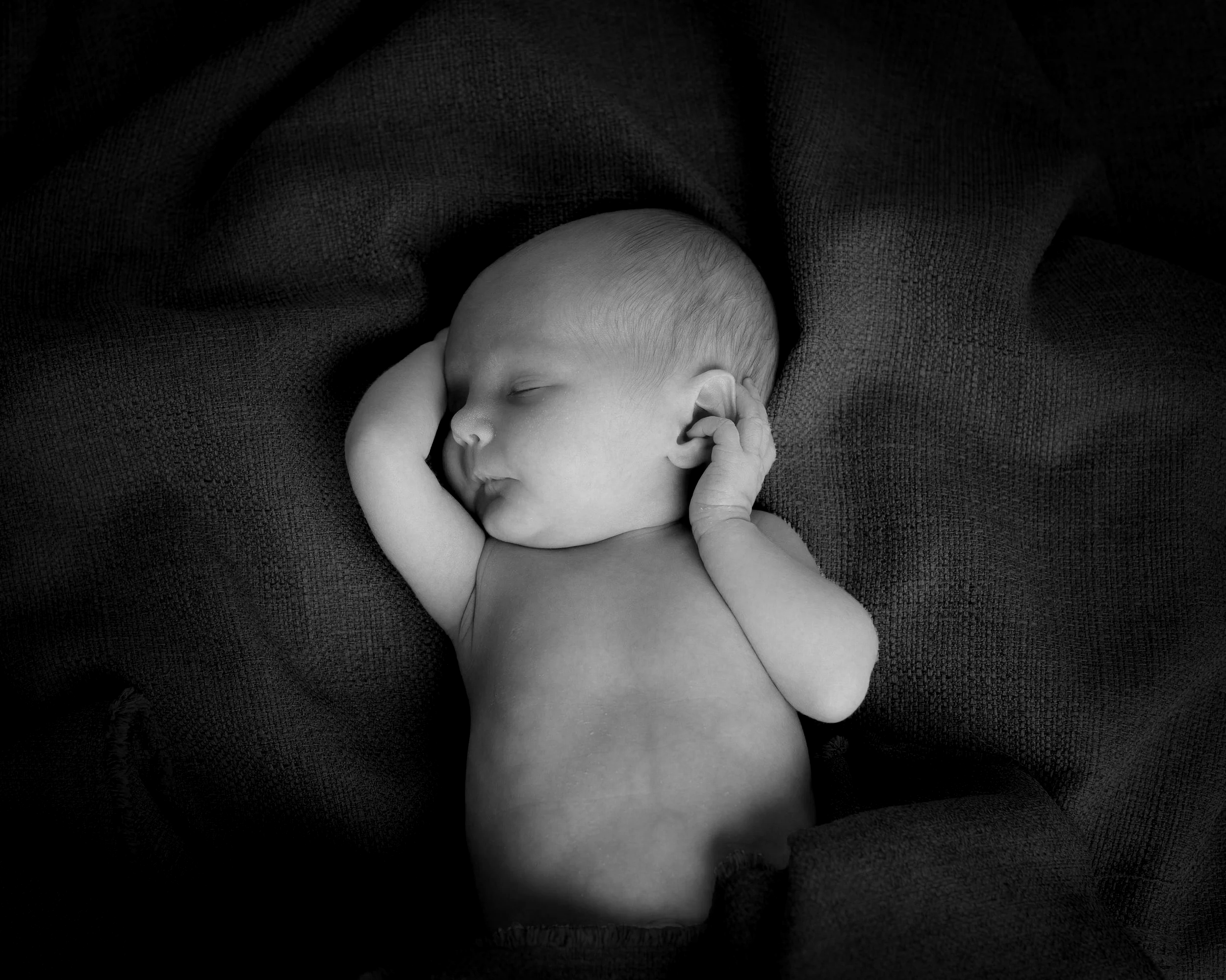 A young child yawning while lying in bed next to a white stuffed animal, wearing a gray knit hat with bear ears.
