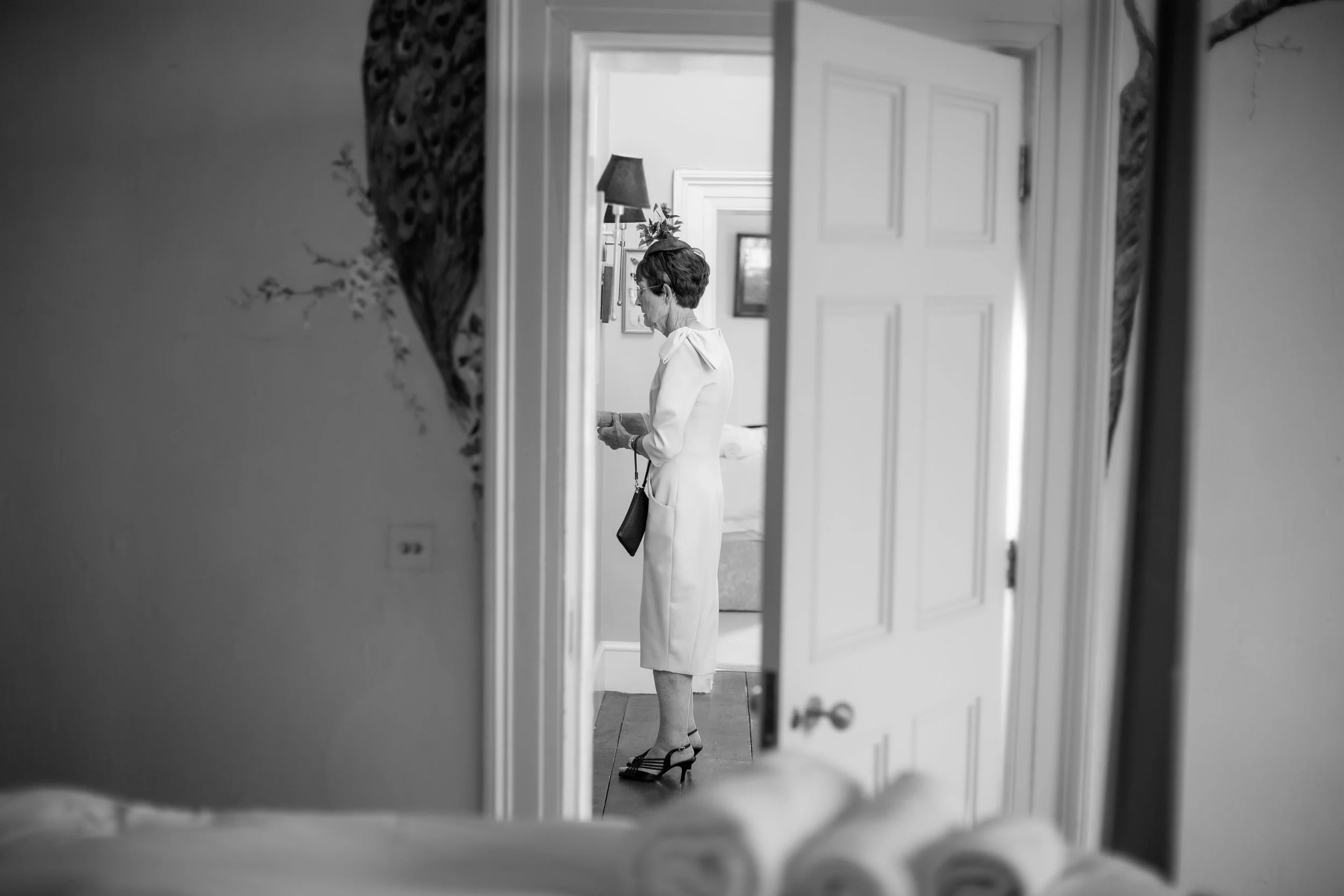 A woman in a white dress and high heels is looking at her phone in a room, as seen through a mirror on the wall.
