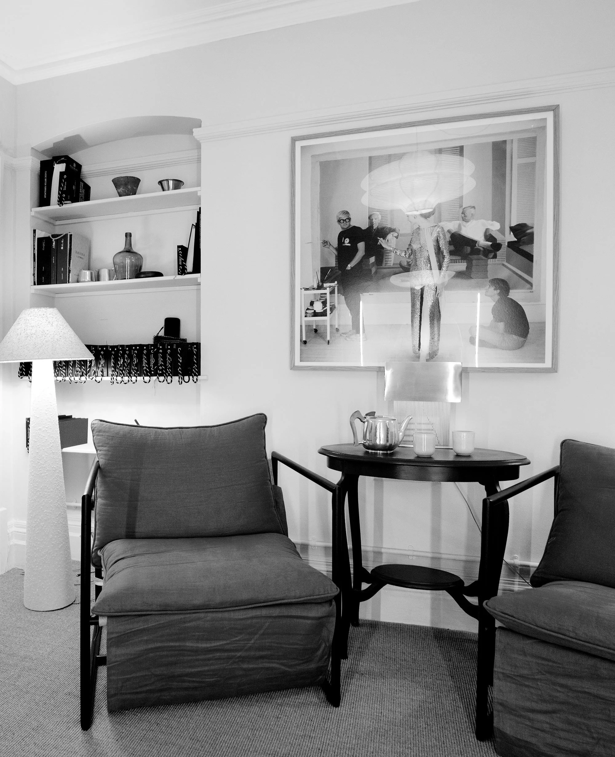 Living room with two armchairs, a small table with a teapot and cups, a floor lamp, and a large framed picture on the wall.
