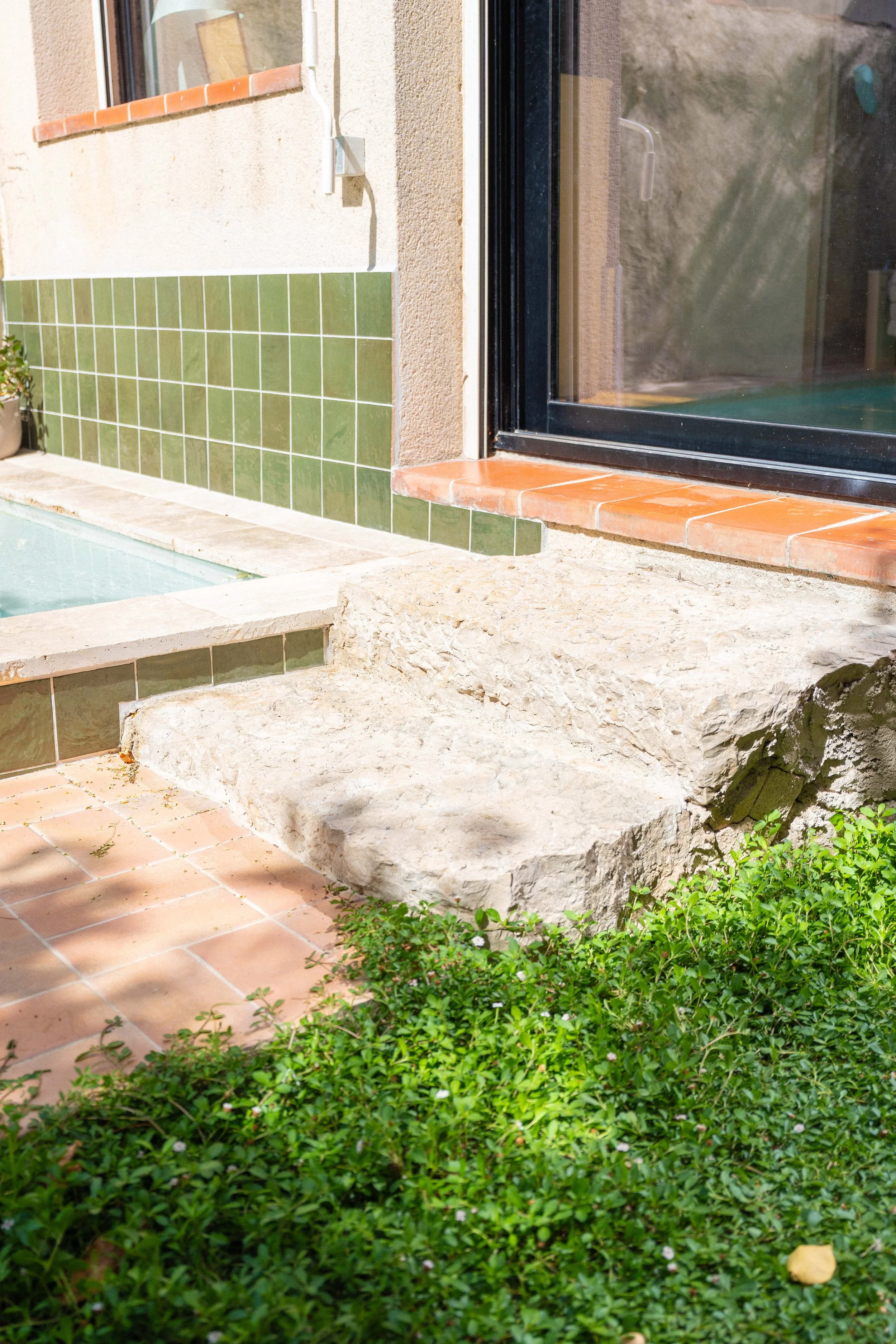 Pierre plate devant une porte-fenêtre en verre, avec des dalles en terre cuite et un mur partiellement carrelé en vert