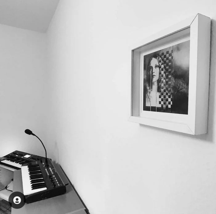 A white wall with a framed abstract artwork and a desk with a keyboard and microphone.