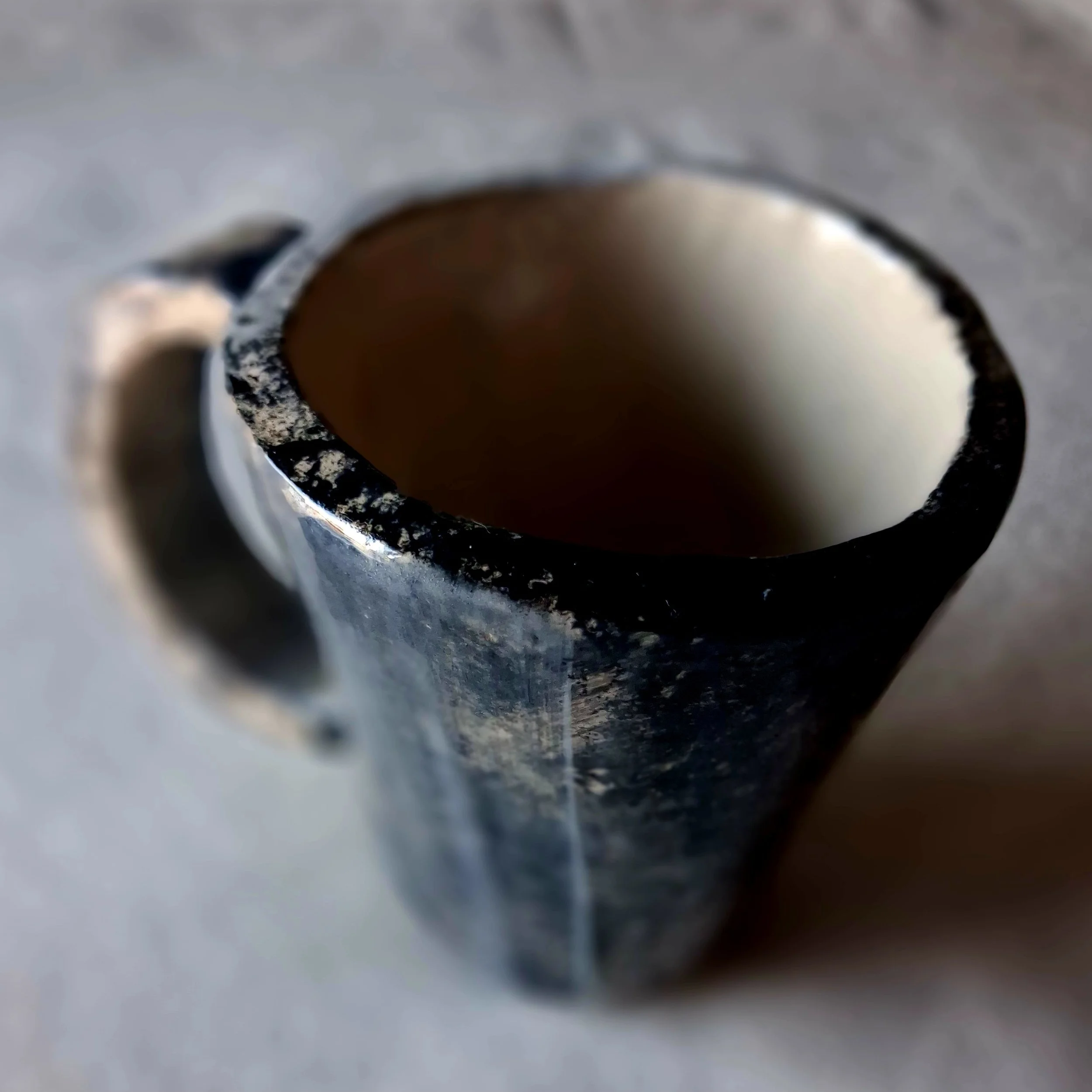Close-up of a black and white textured ceramic cup with a white interior, viewed from above, on a gray surface.