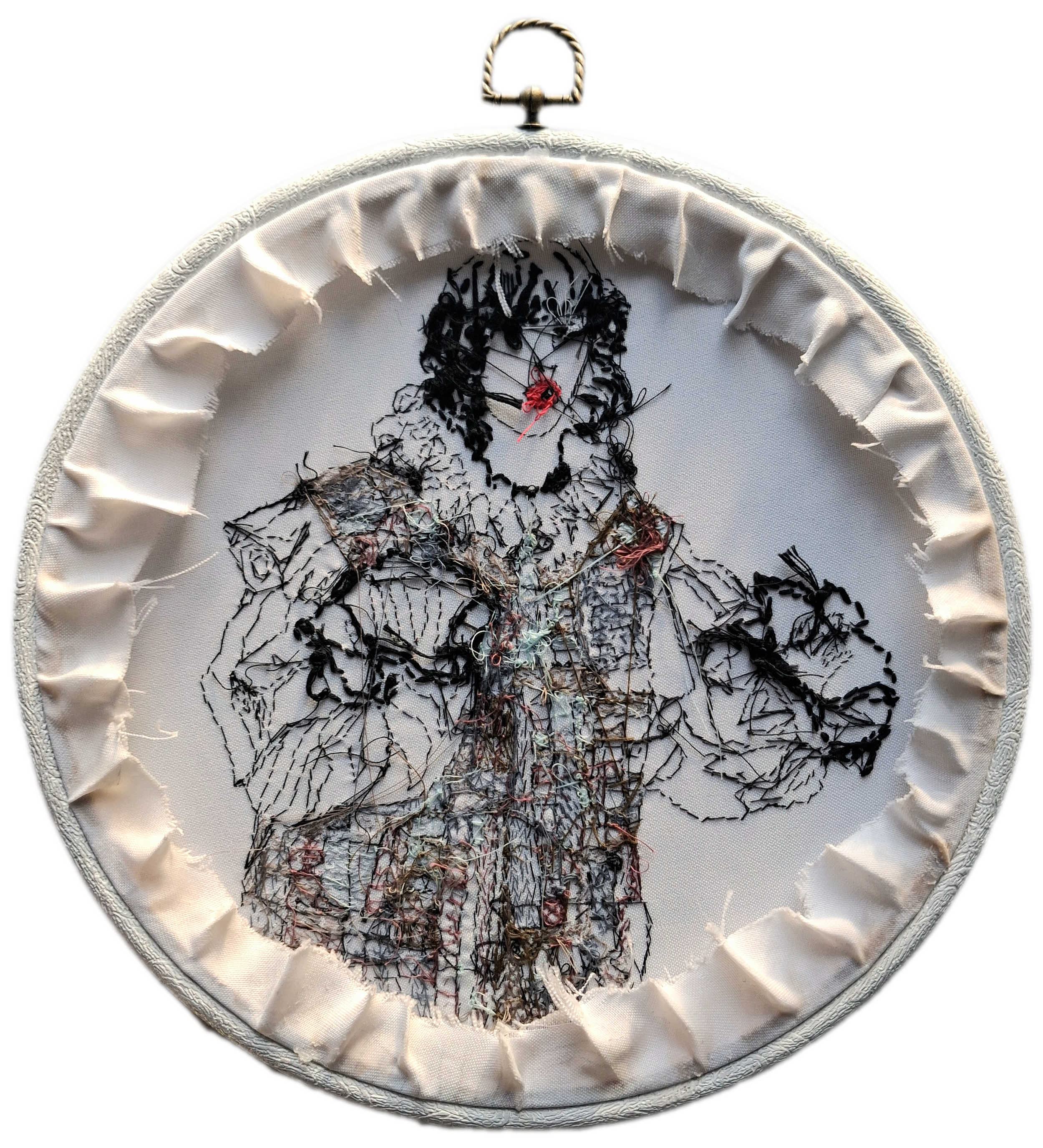 Embroidery hoop with fabric containing a stitched portrait of a woman's face, featuring black and colored threads, surrounded by white ruffled fabric.