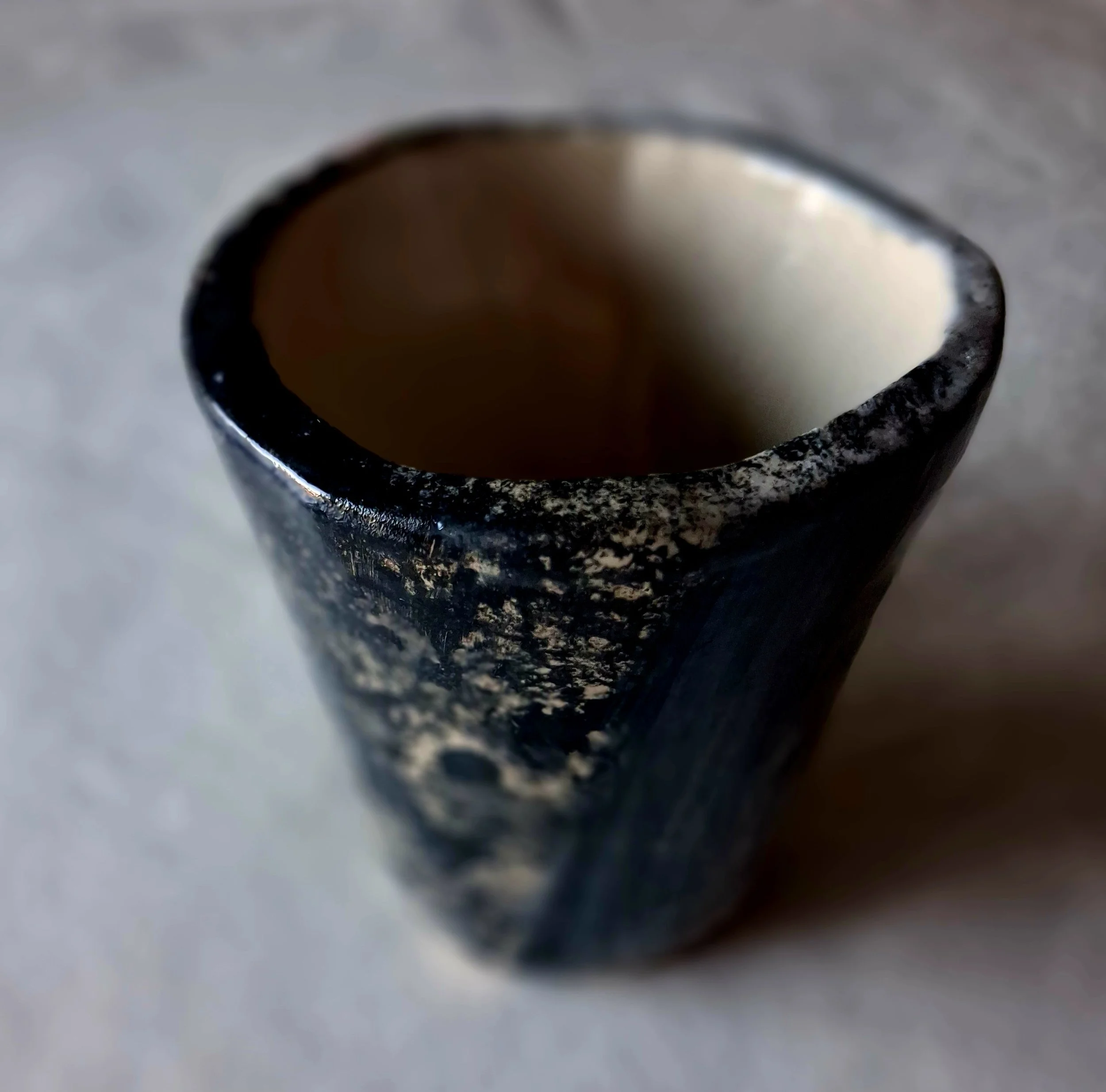 Close-up of a black and white textured ceramic cup with a white interior, viewed from above, on a gray surface.