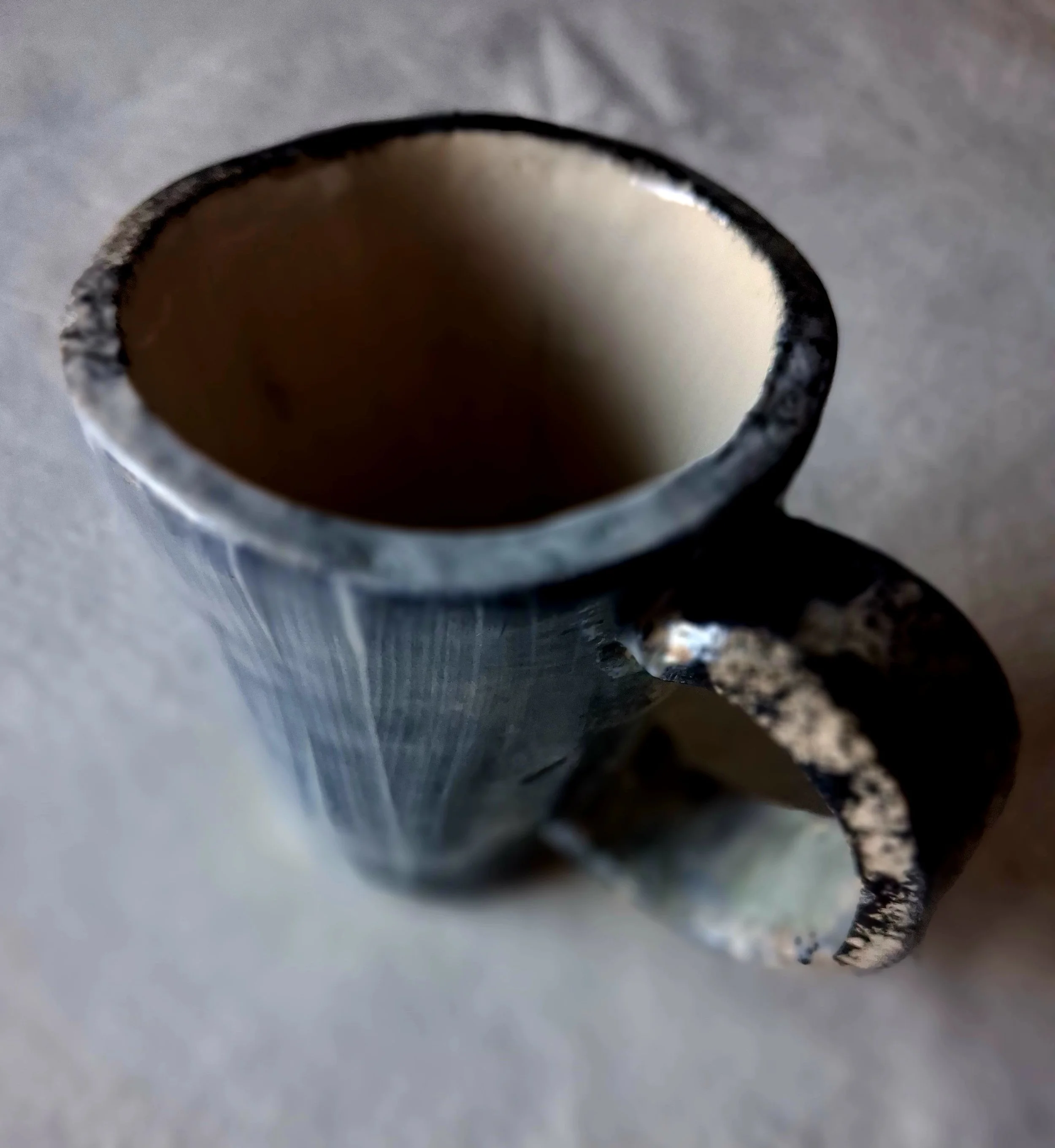 Close-up of a black and white textured ceramic cup with a white interior, viewed from above, on a gray surface.