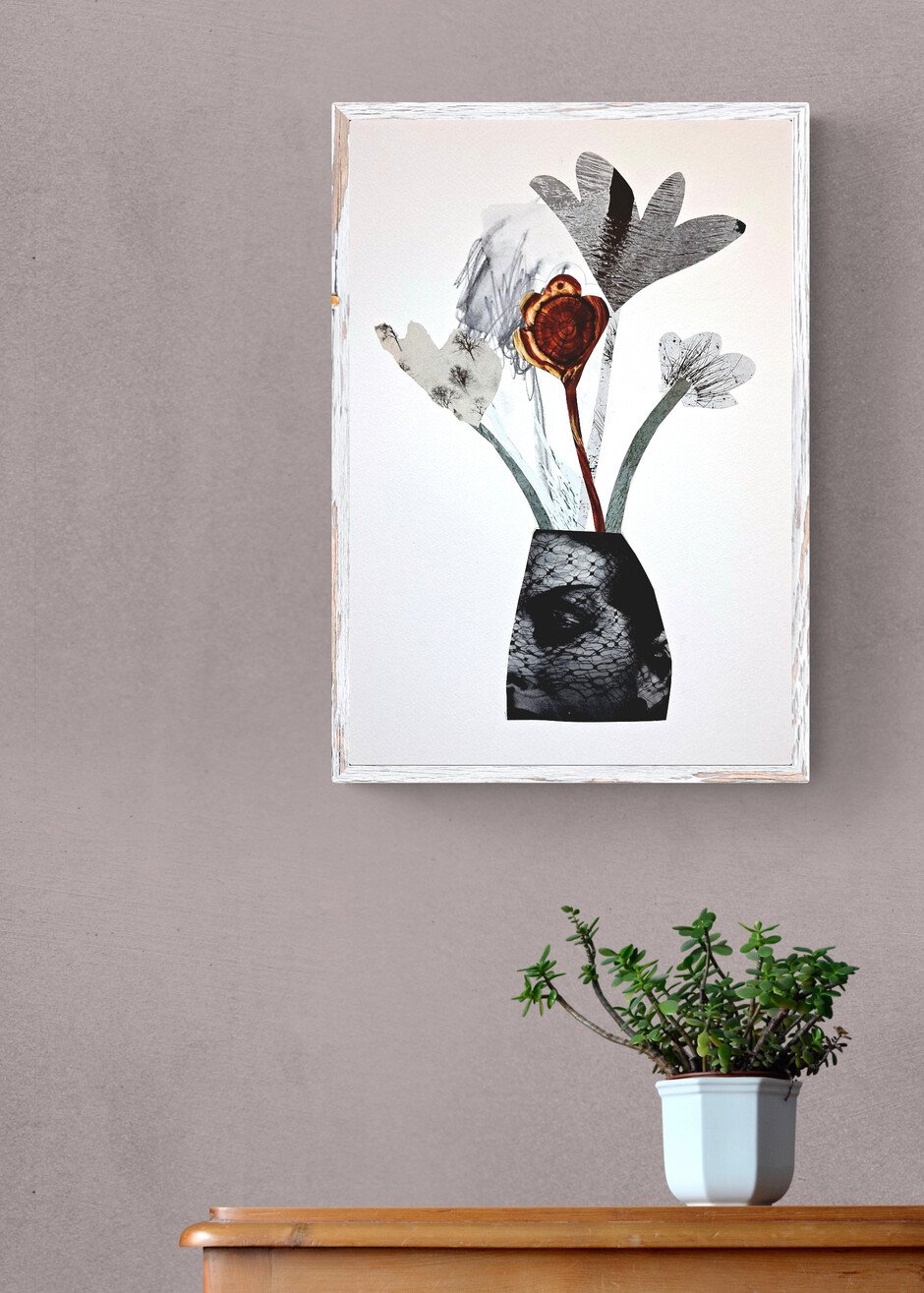 A framed artwork of a vase with abstract floral elements hangs on a light gray wall, with a potted plant with green succulent foliage on a wooden surface below.