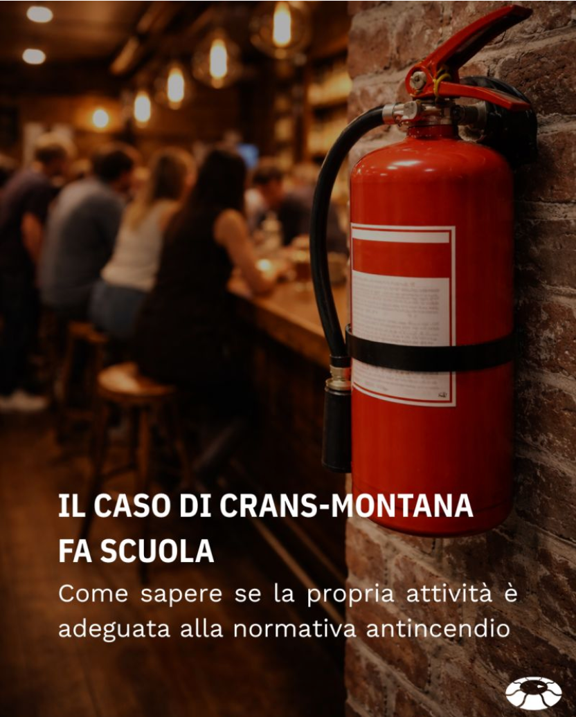 A fire extinguisher mounted on a brick wall in a dimly lit restaurant or bar with people sitting at a bar in the background.