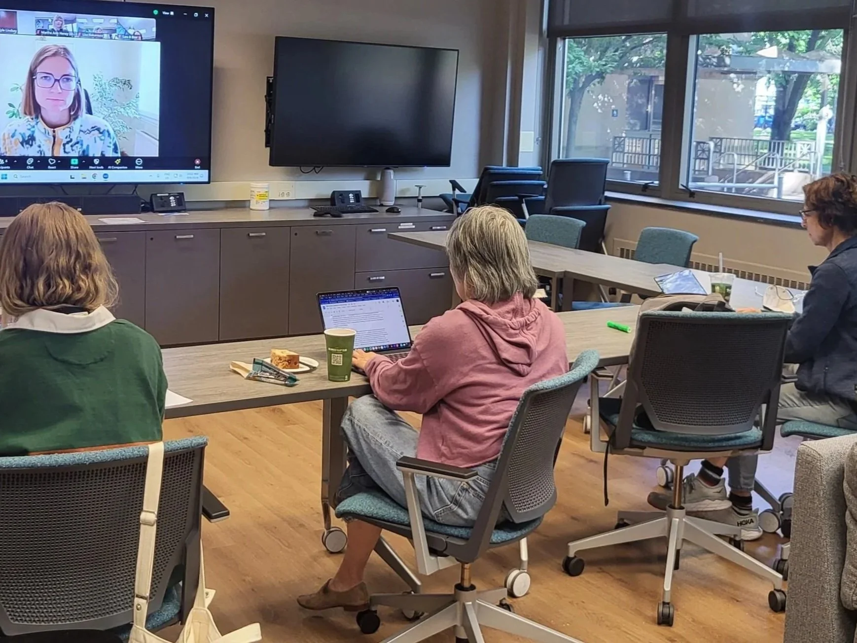 Three researchers working together on laptops during a facilitated collaborative writing sprint, with the facilitator joining remotely.