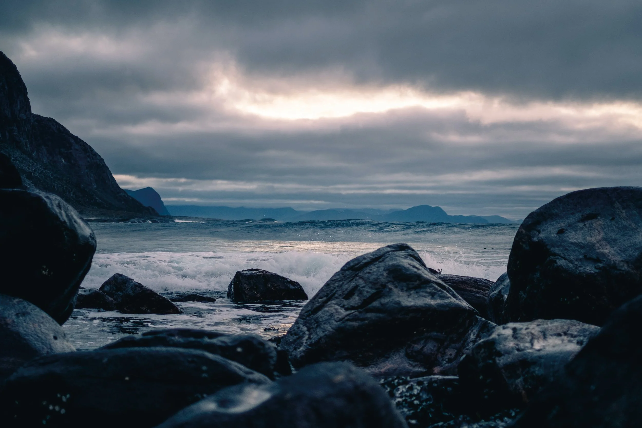 Rocky shoreline with ocean waves crashing under a cloudy sky.