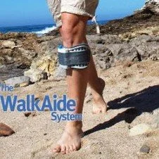 Person walking barefoot on a rocky beach wearing shorts with a beach background.