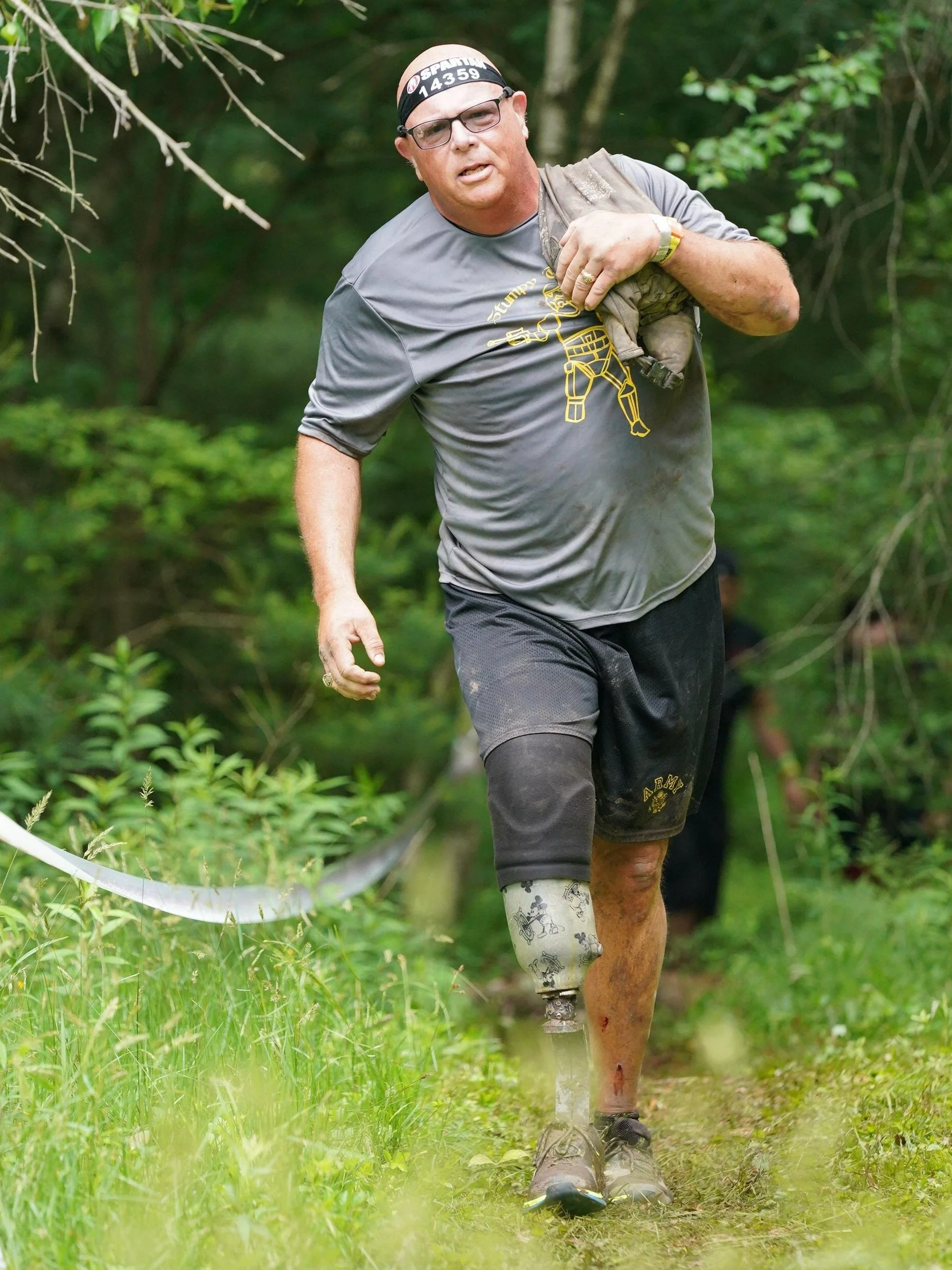 A man with a prosthetic leg running through a forested trail during a race or outdoor activity.