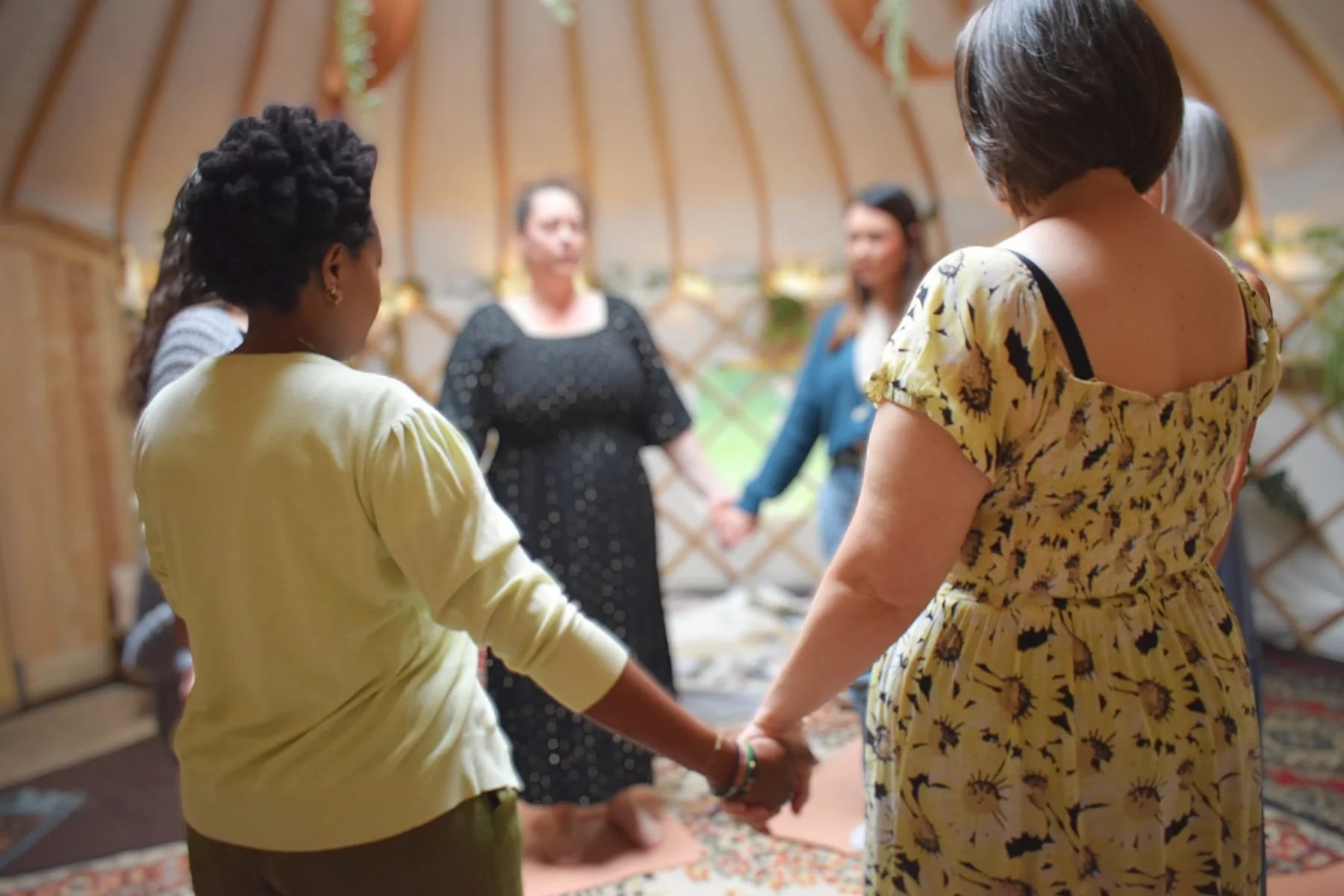 People standing in a circle with their hands together at a sister circle lead by Zanny Jode