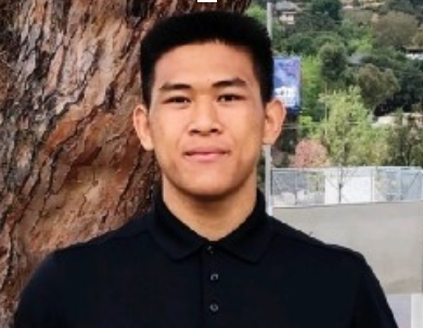 Person standing in front of a tree and outdoor scenery wearing a black shirt.