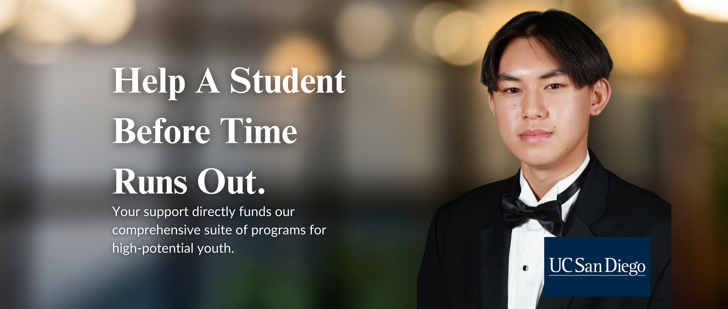 A young woman with curly hair wearing a Harvard sweatshirt, pointing to the Harvard crest on her chest, smiling confidently, with a blurred background.
