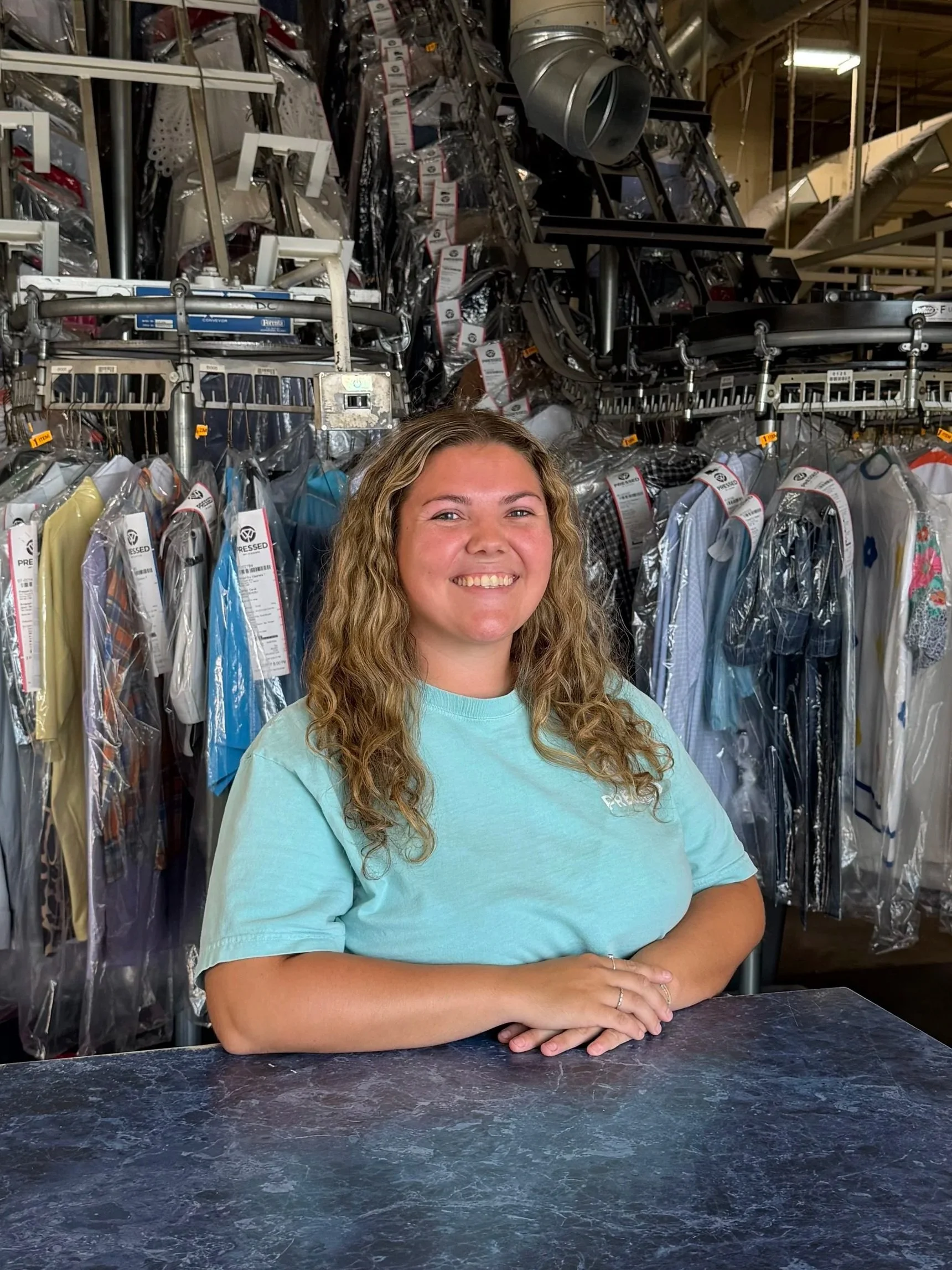 Lauren Uncel smiling at the camera, seated at a desk with a computer, at Pressed Dry Cleaners in Wichita Falls, TX.
