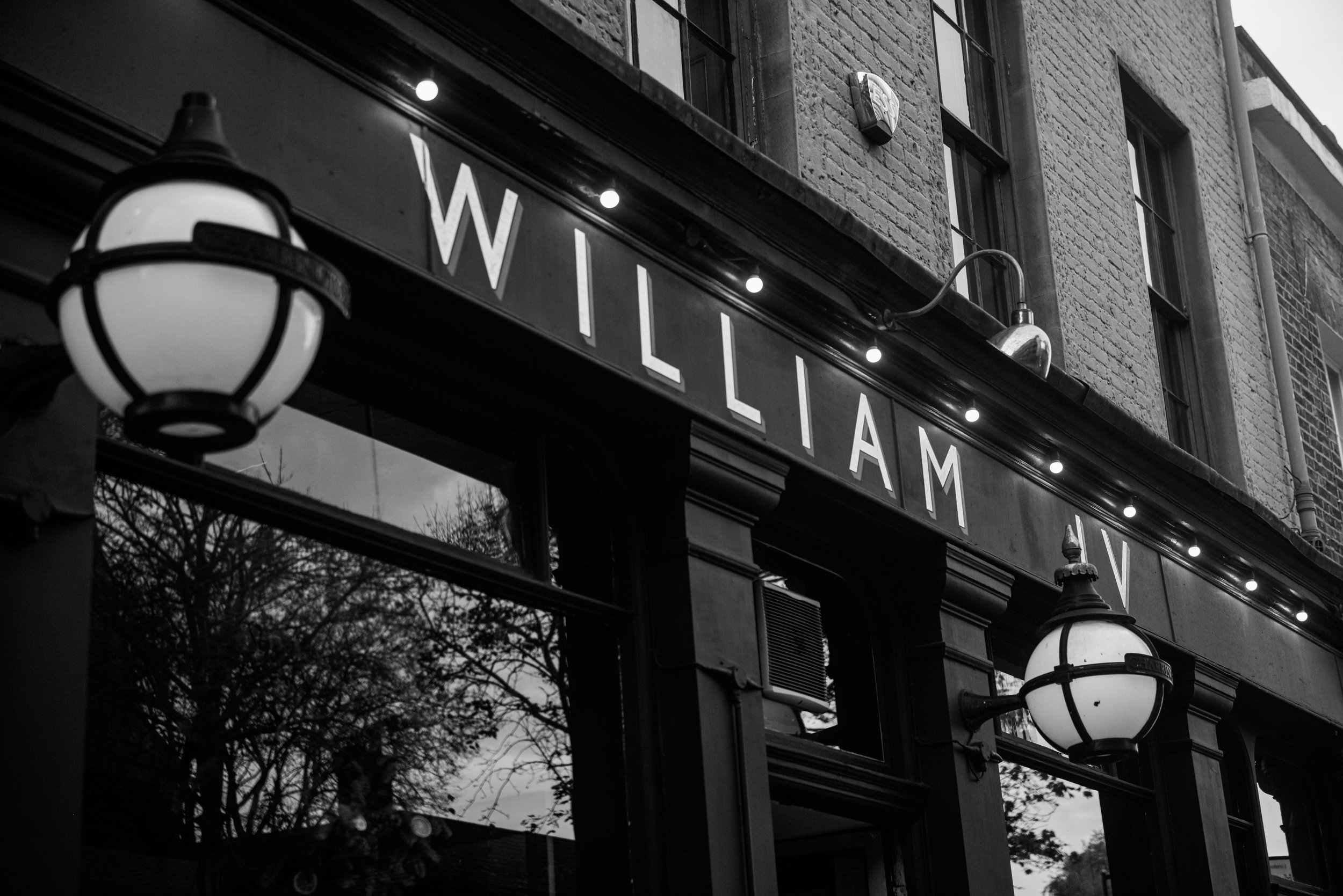 Black and white photo of a storefront with the sign 'WILLIAM' and two hanging lamps outside