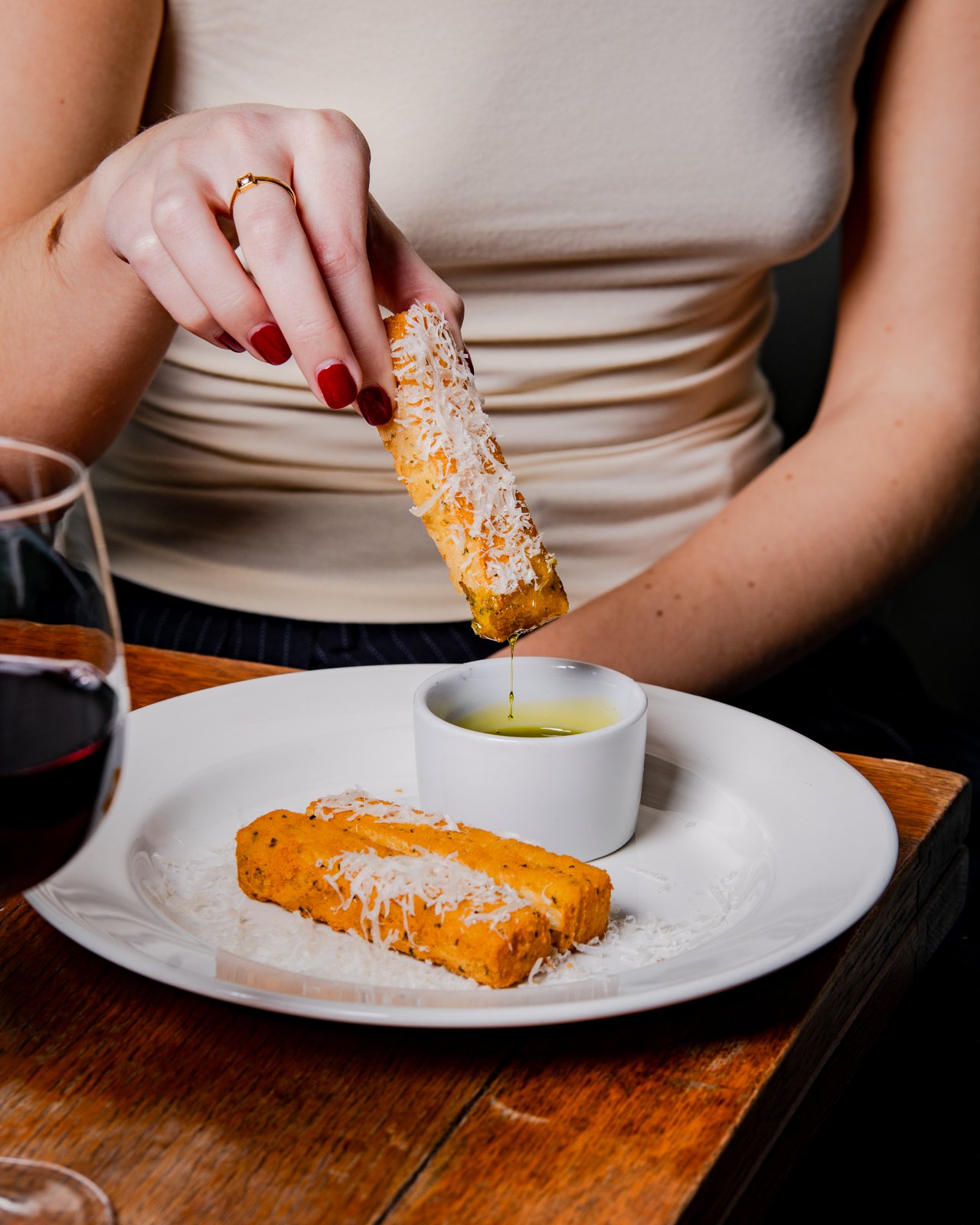 Woman dipping a cheese-stuffed breadstick into olive oil on a white plate.