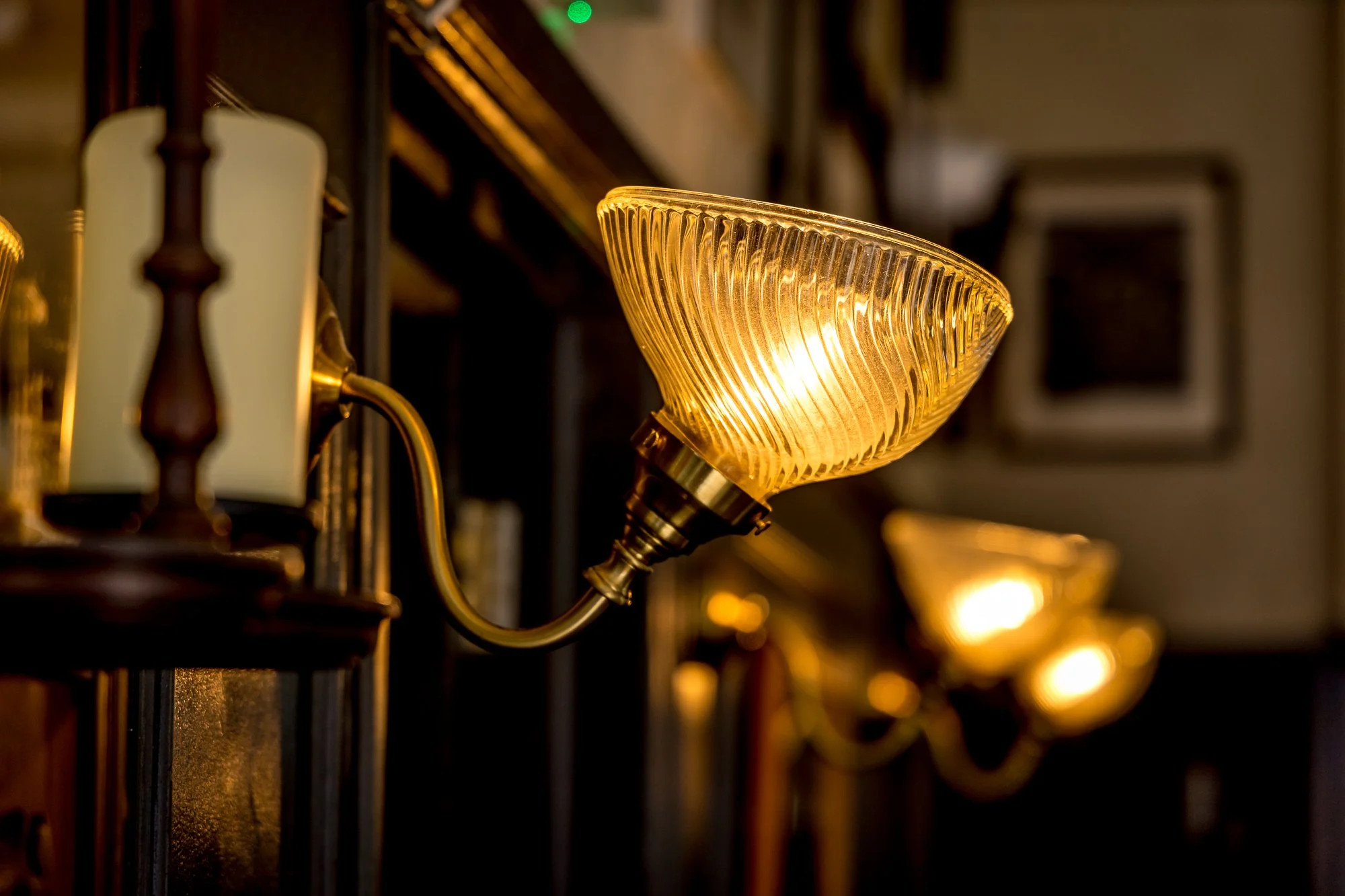 A row of vintage brass wall sconces with glass shades emitting warm light, mounted on a dark wooden wall.