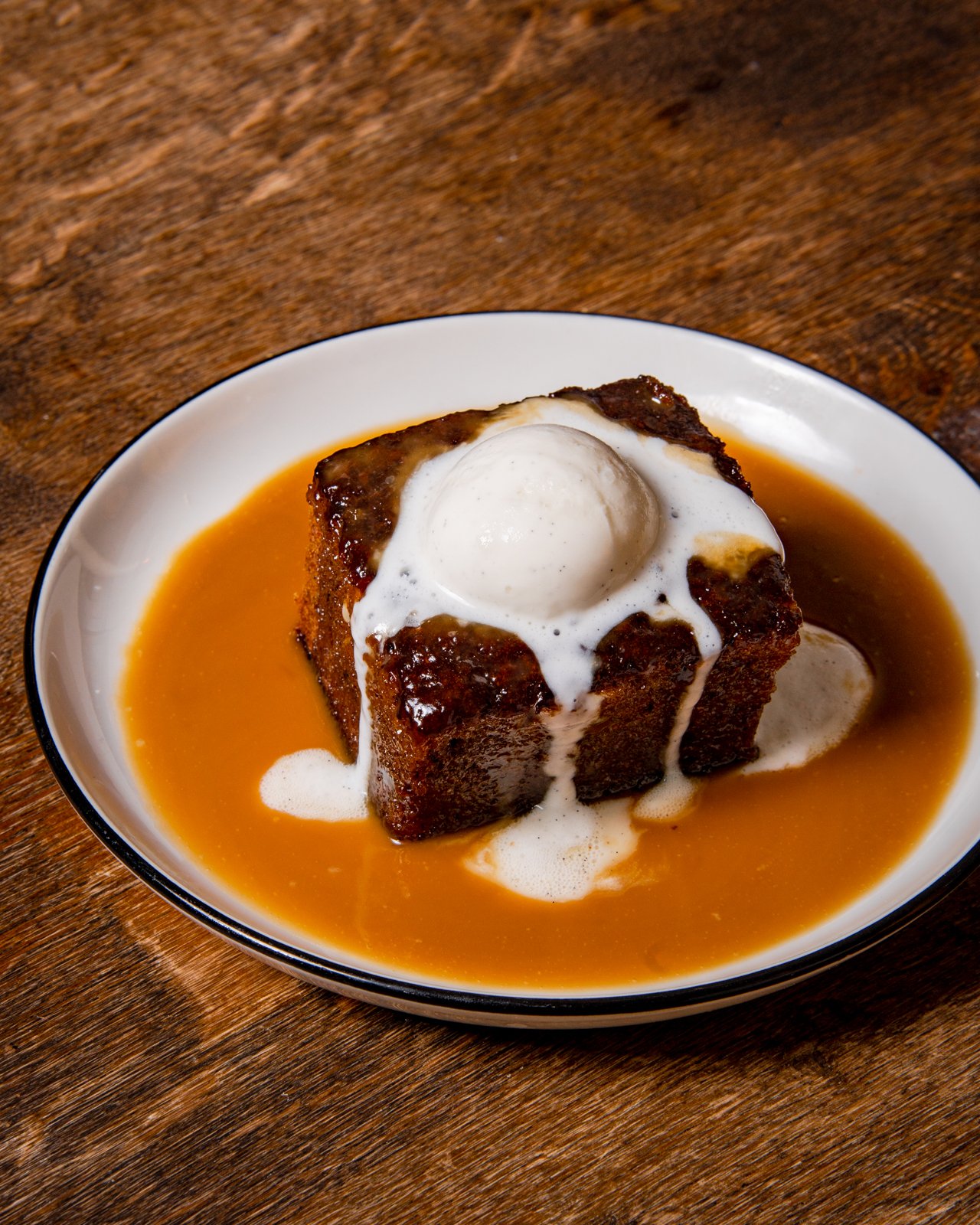 French toast casserole topped with a poached egg, served with syrup on a white oval dish on a wooden surface.